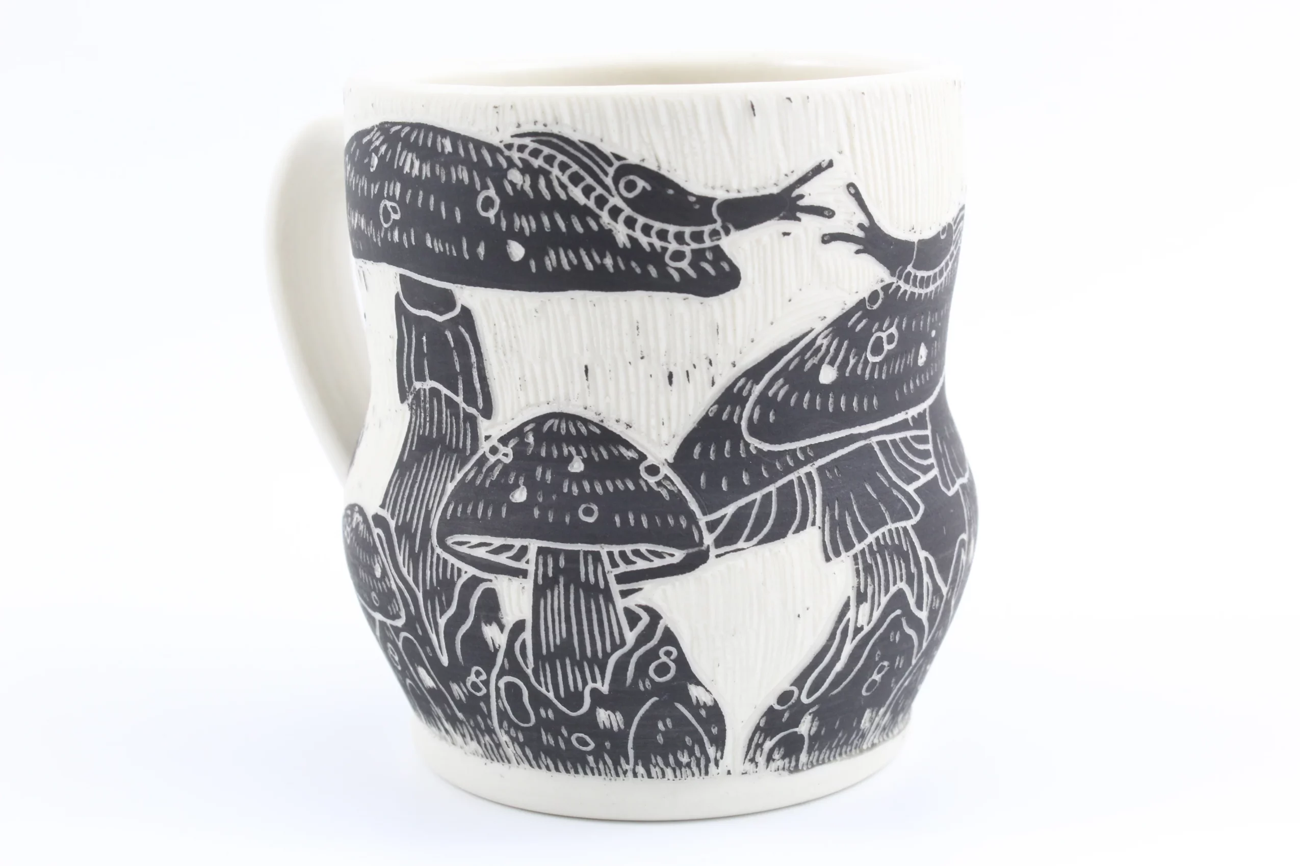 White mug with black illustrations of frogs and mushrooms, detailed and stylized, on a white background.