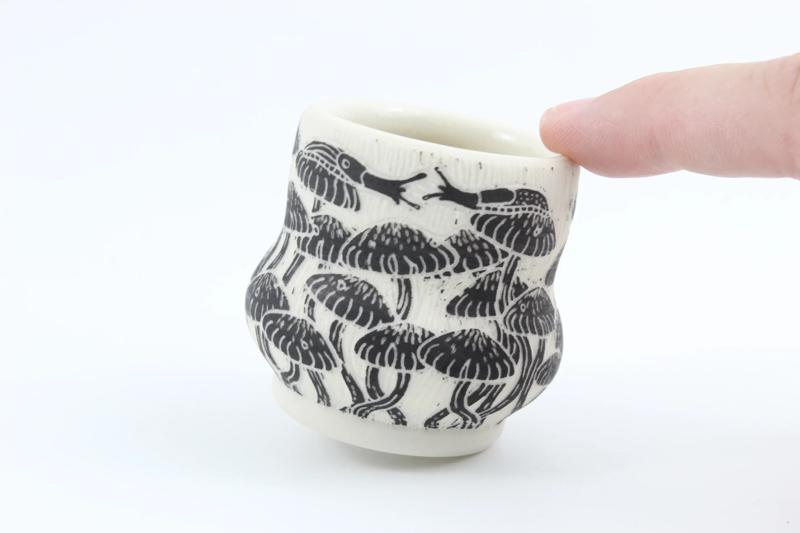 Small ceramic cup with black scorpion patterns, held by a person's finger, against a white background.
