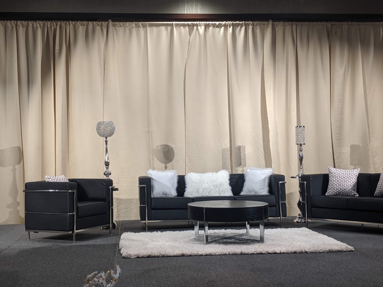 Living room with black sofas, white pillows, a white rug, and curtains in the background.