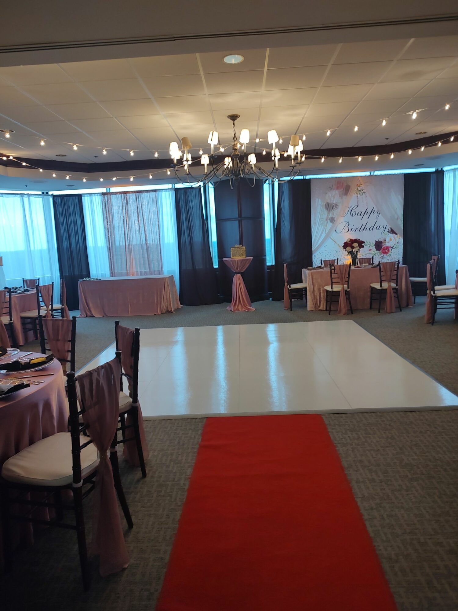 Room with tables, chairs, and decorations, viewed from a tilted angle, with a red carpet on the right side.