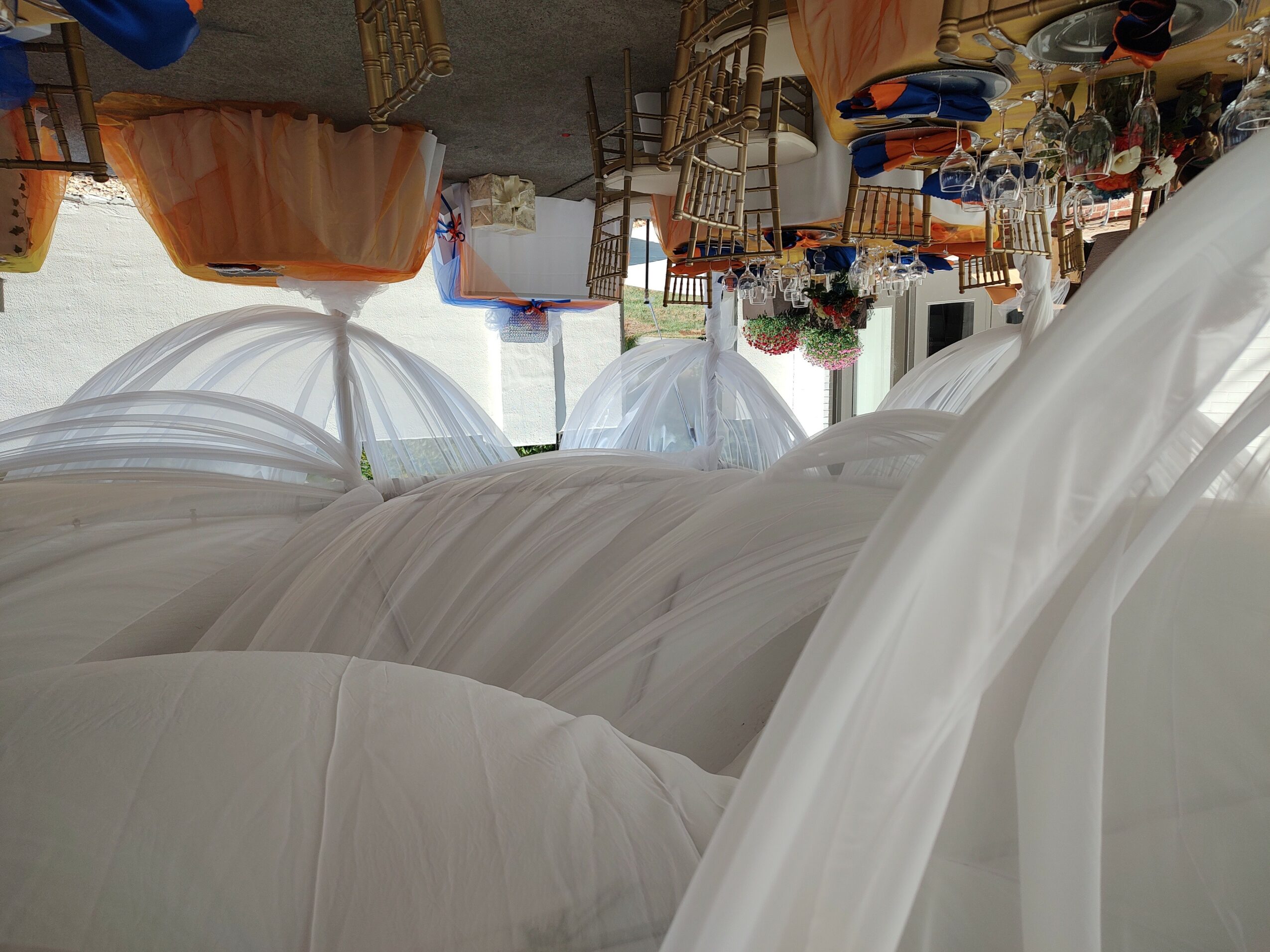 Event setup with white draped fabric, tables, chairs, and decorations in a bright room.