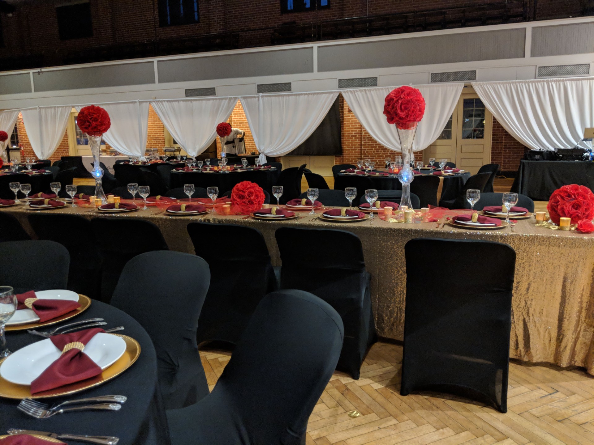 Event banquet setup with tables, chairs, and floral centerpieces, decorated with drapes and tableware.