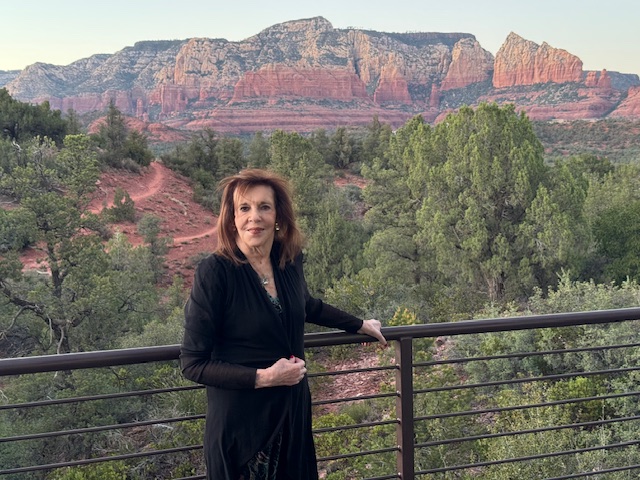 Woman standing by a railing with a canyon landscape and trees in the background.