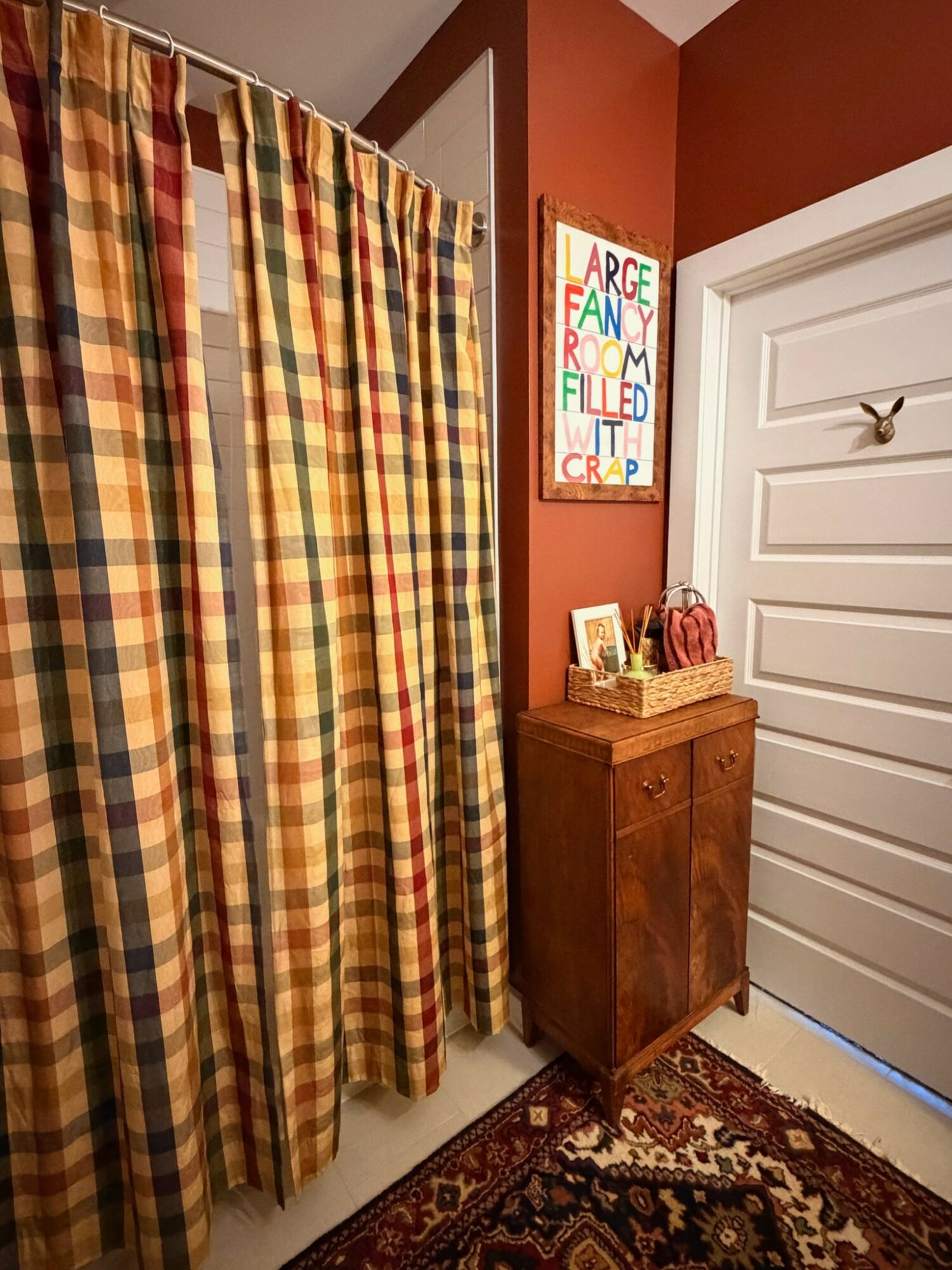 Corner of a room with a colorful plaid curtain, a small wooden cabinet, and a framed art piece on a red wall.