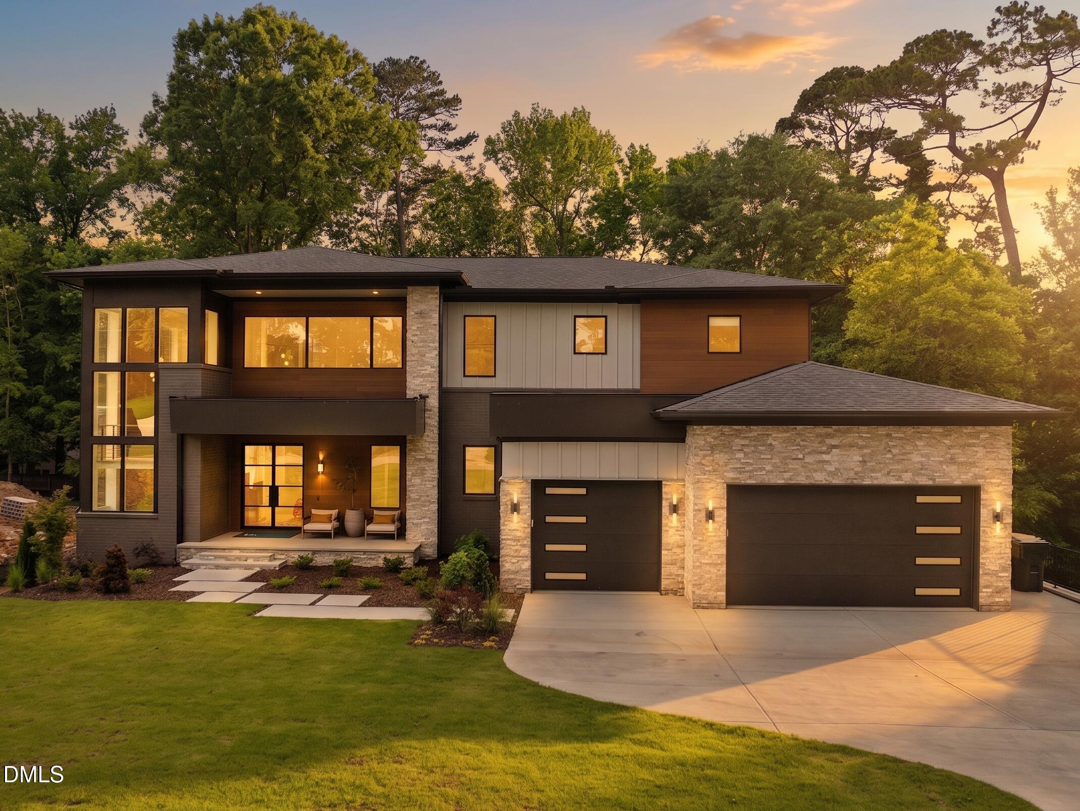 Modern two-story house with large windows, a two-car garage, surrounded by trees and a well-maintained lawn.