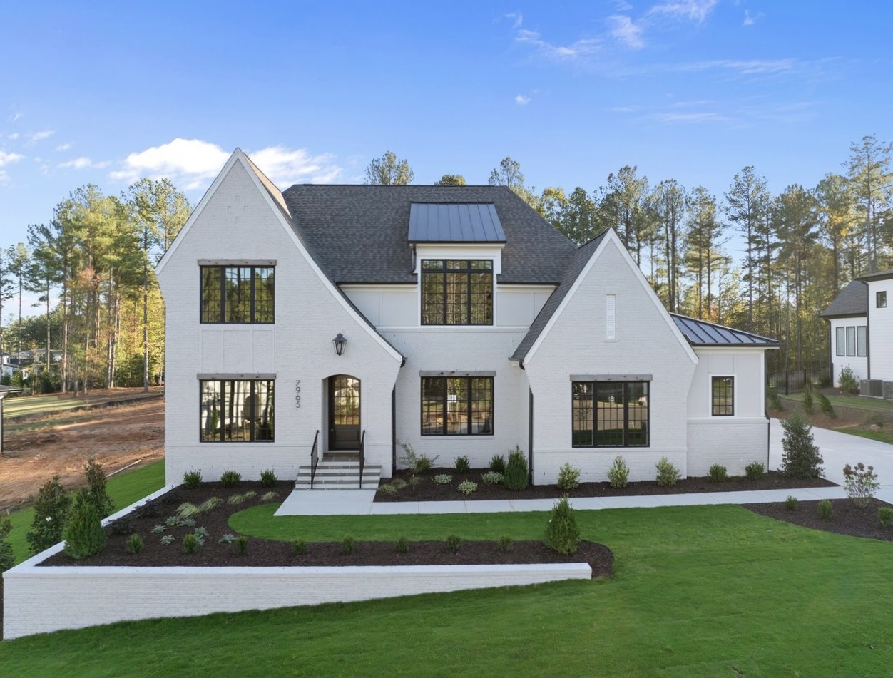 Modern two-story house with white exterior, black roof, large windows, and landscaped front yard with lawn and shrubs.