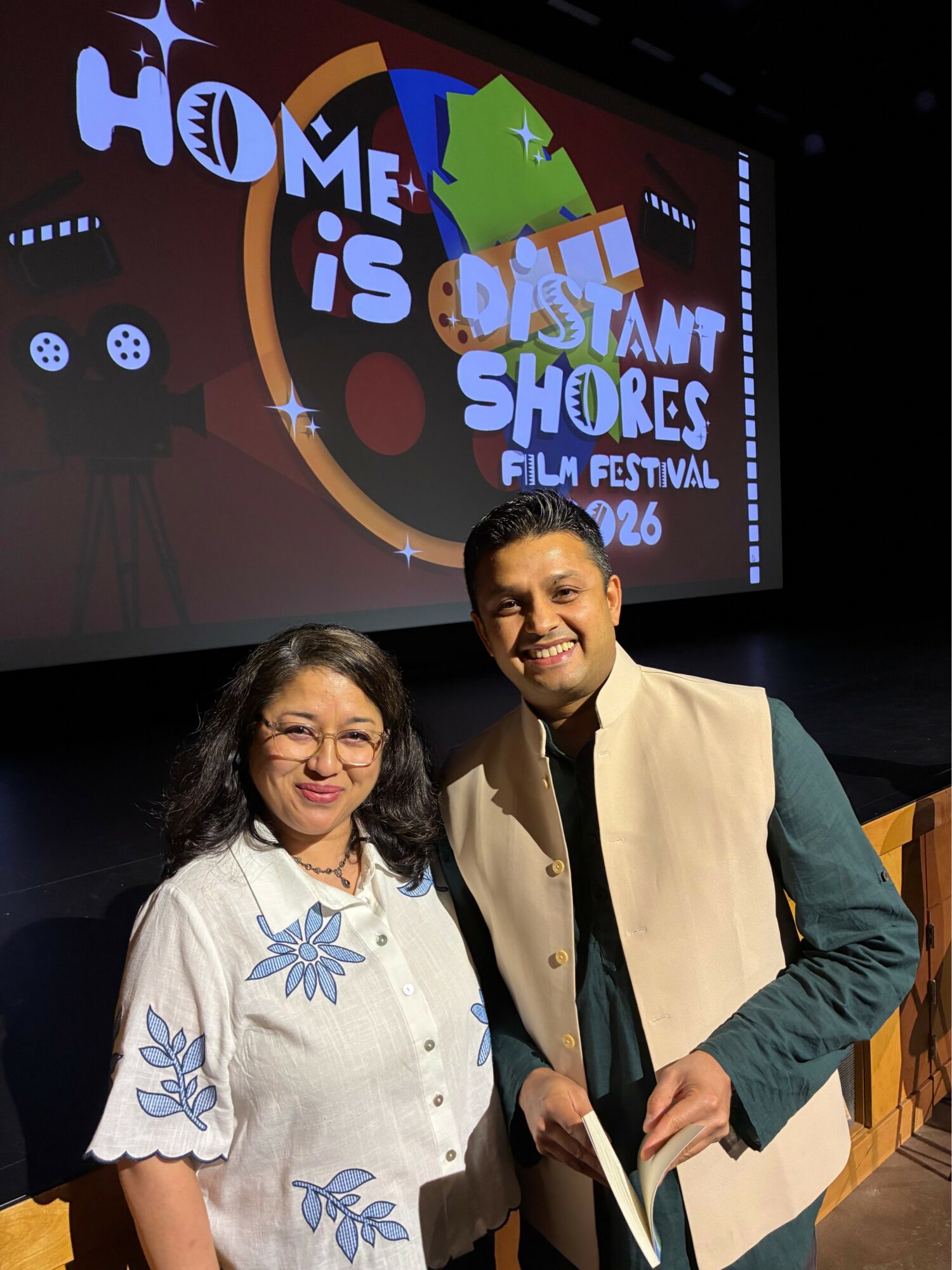 Two people standing in front of a screen with a colorful logo for a film festival, smiling at the camera.