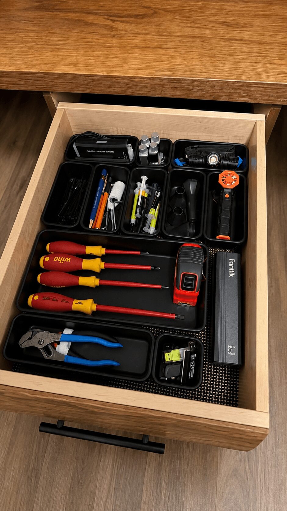 Open drawer with various tools including screwdrivers, pliers, and a flashlight, organized in black cases inside a wooden drawer.
