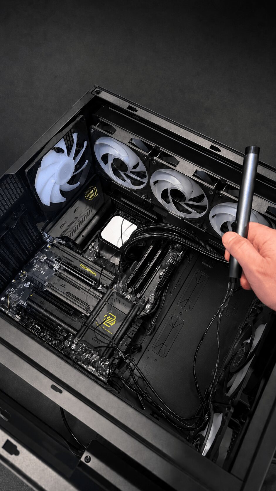 Person installing or repairing a computer's internal components with a screwdriver, inside a black case with cooling fans visible.