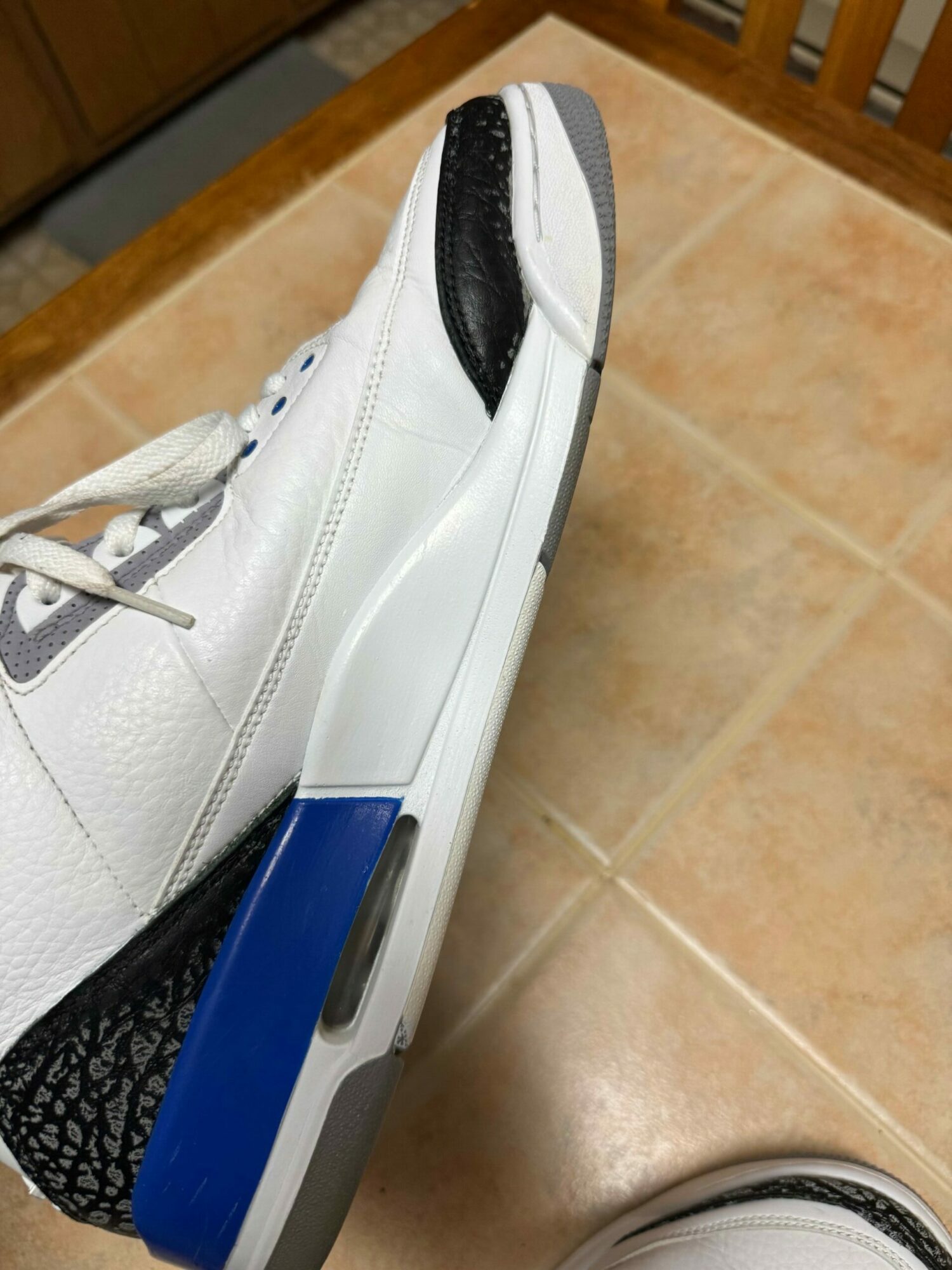 White athletic shoe with black and blue accents on a tiled floor.