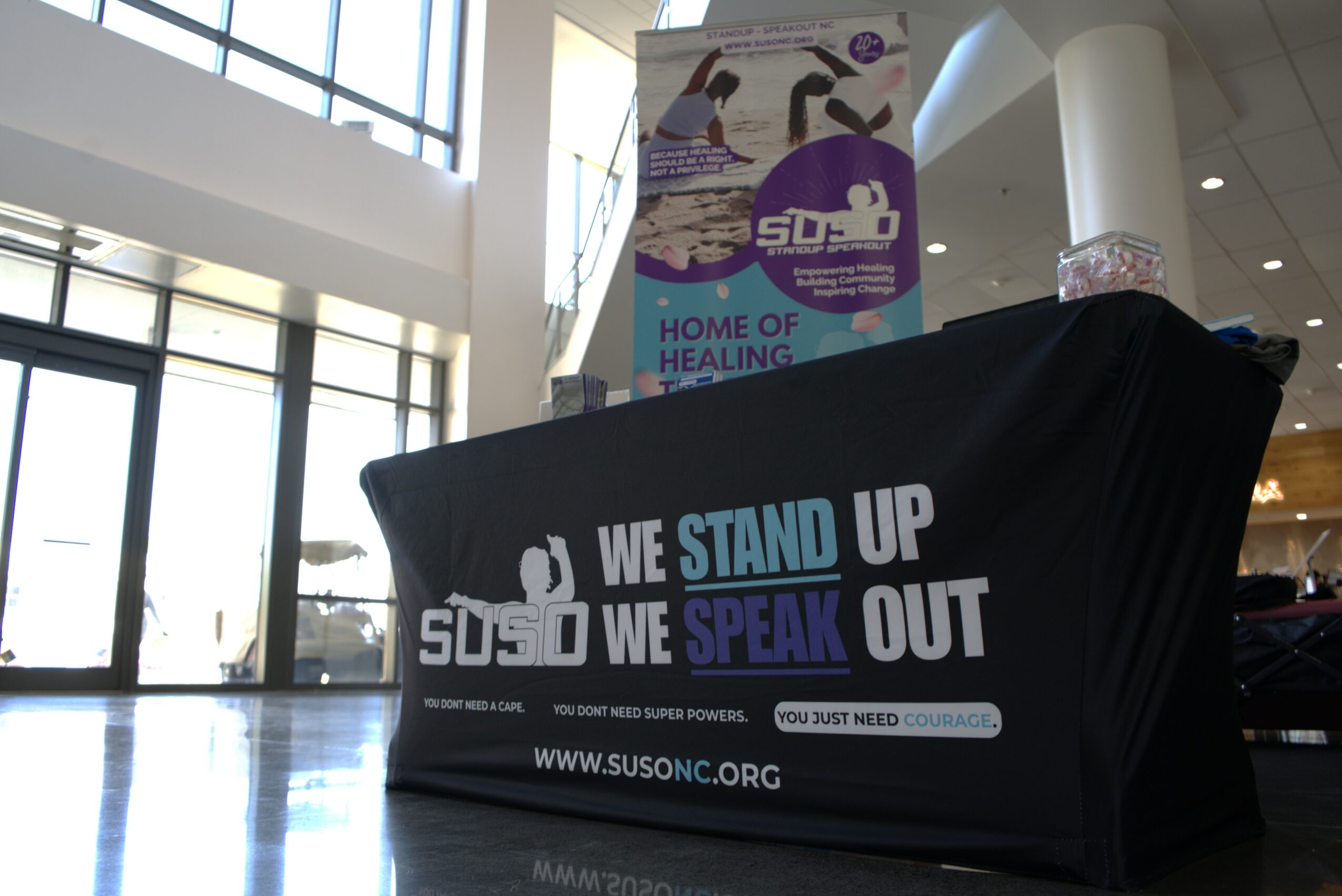 Table with a black cover displaying text about standing and speaking, in a spacious indoor area with large windows.