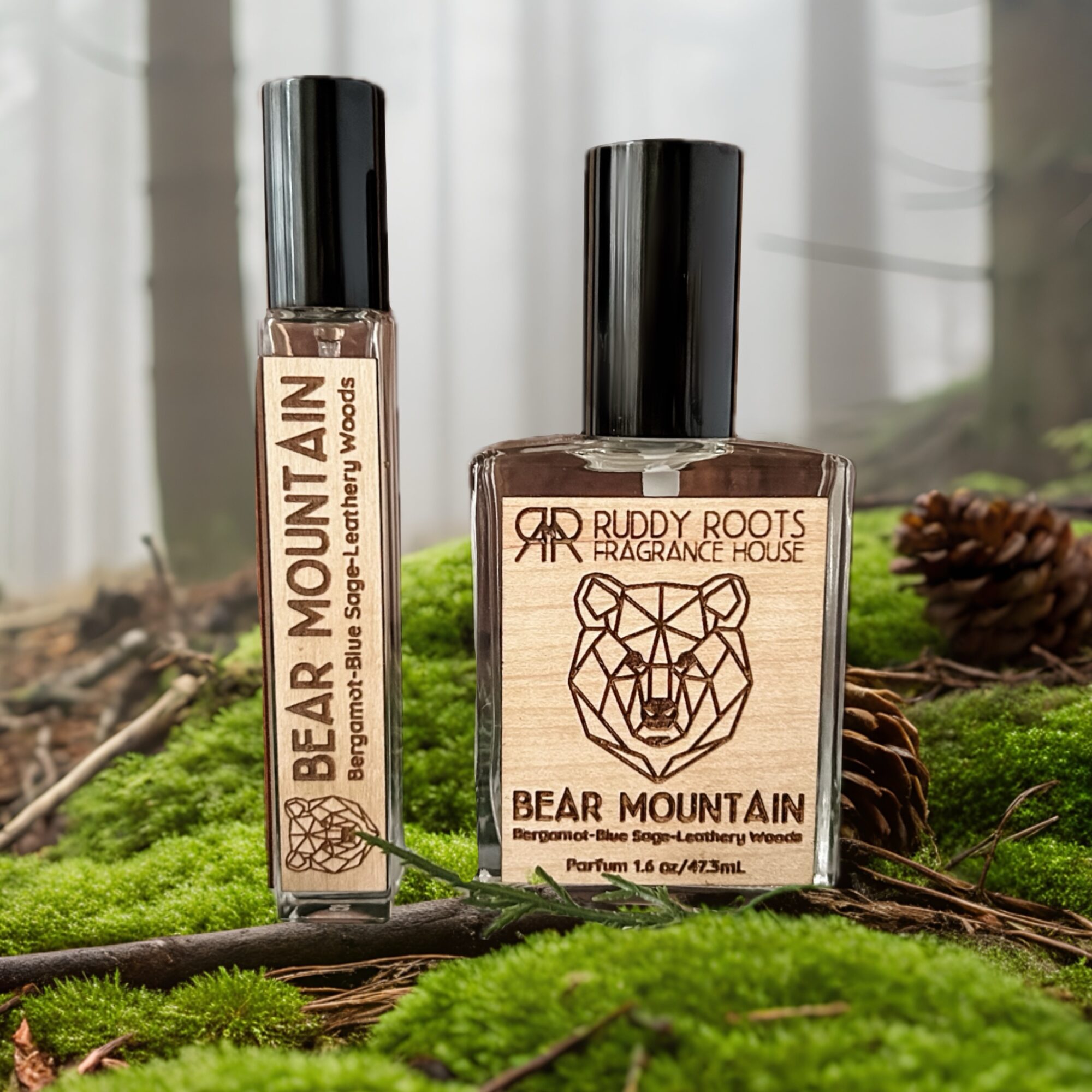 Two bottles of fragrance spray on mossy ground with pinecones, one labeled Bear Mountain and the other Ruddy Roots, in natural light.