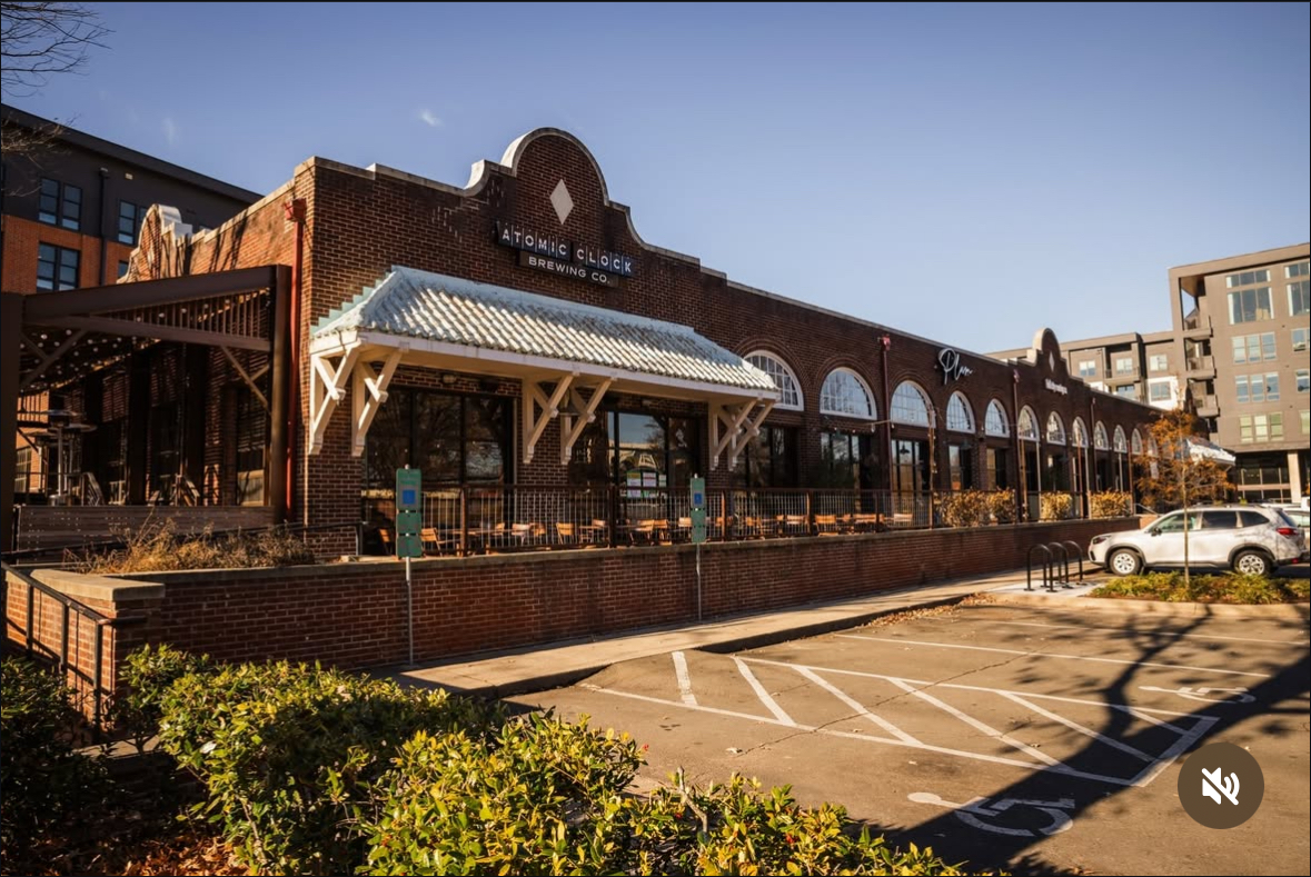 Brick building with arched windows and a metal awning, parking lot in front, clear sky background.
