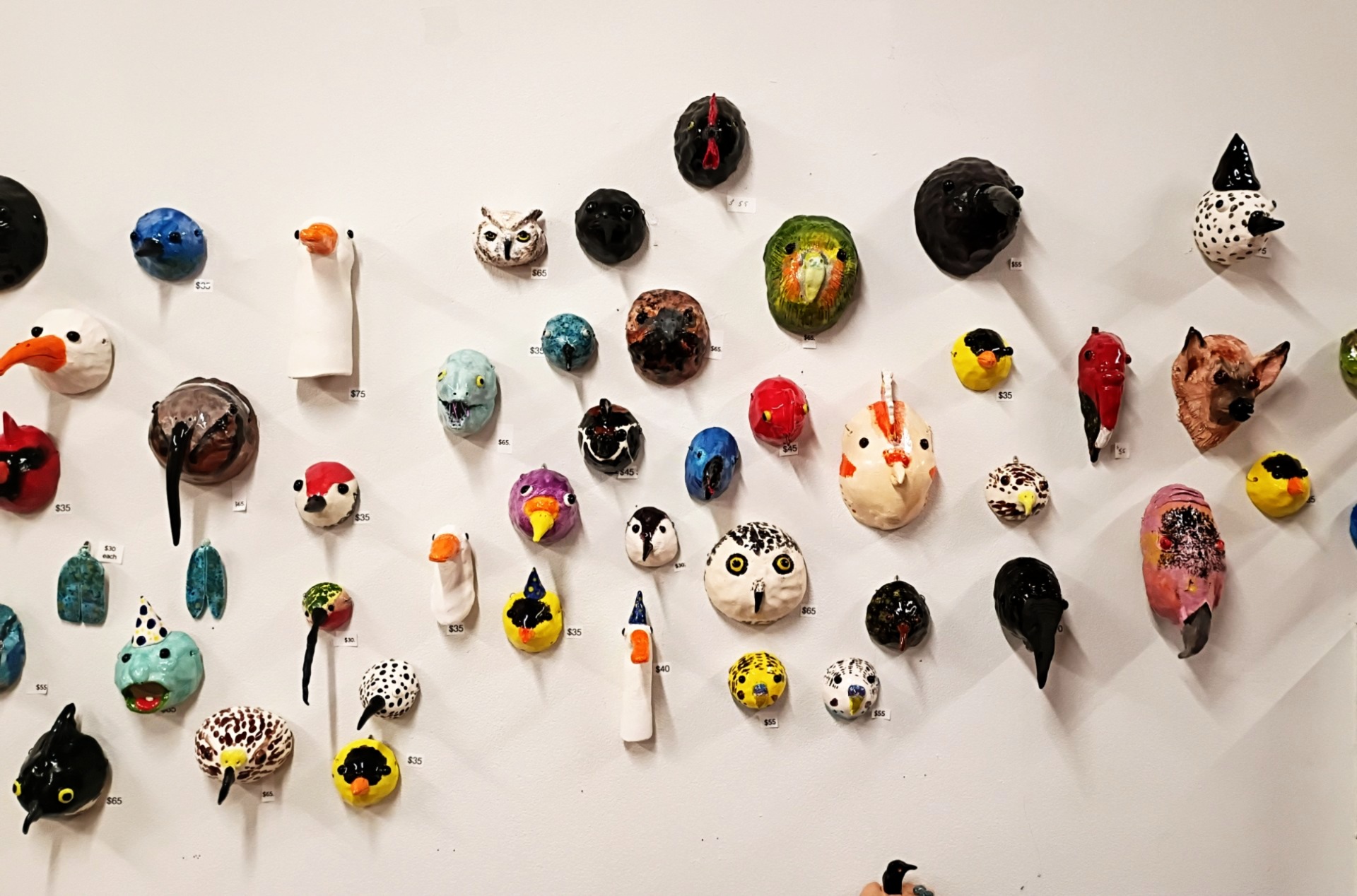 Collection of small, colorful, handcrafted animal and face sculptures mounted on a white wall.