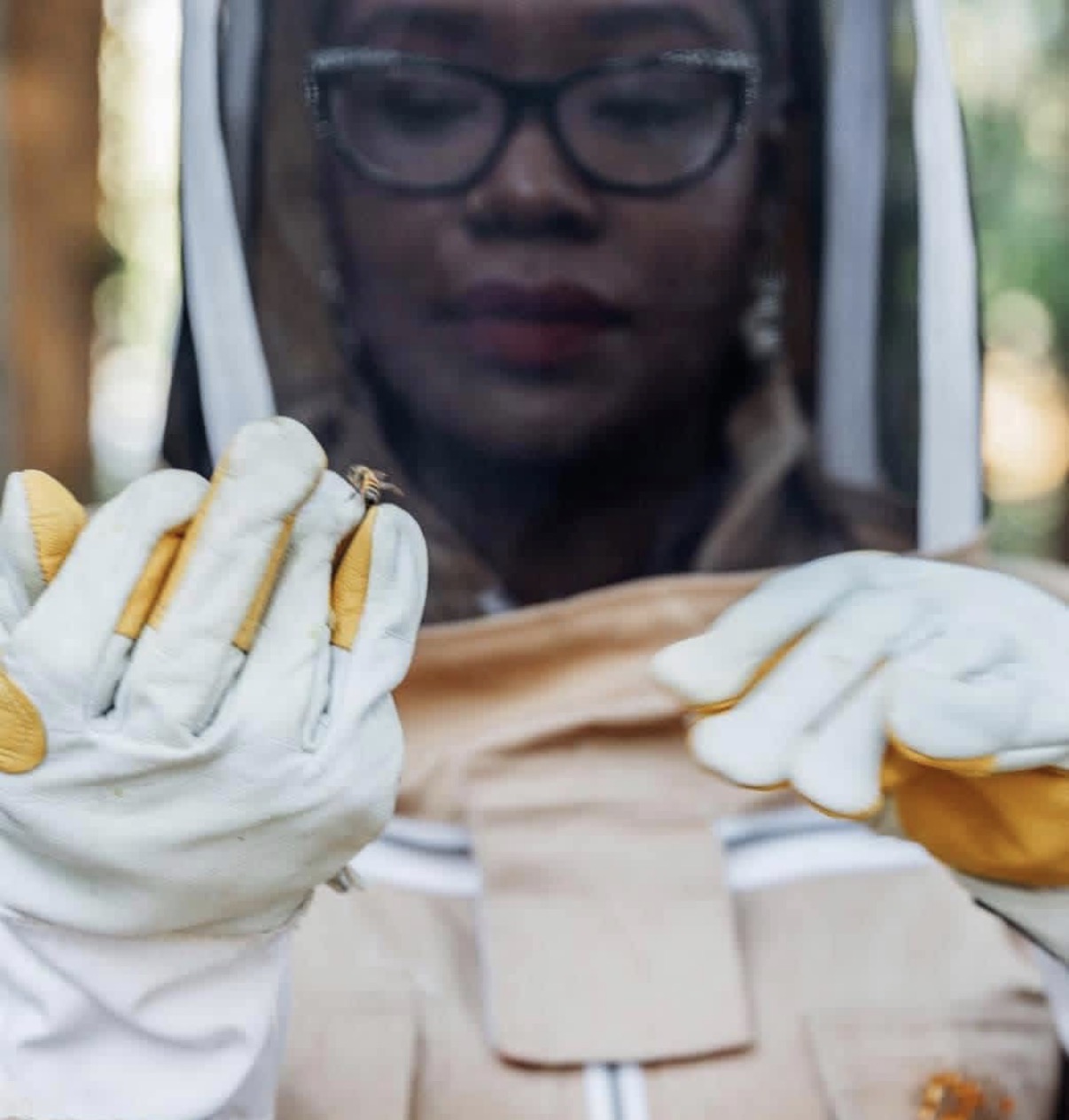 Person wearing protective gear examines a small object with gloves and a face shield.