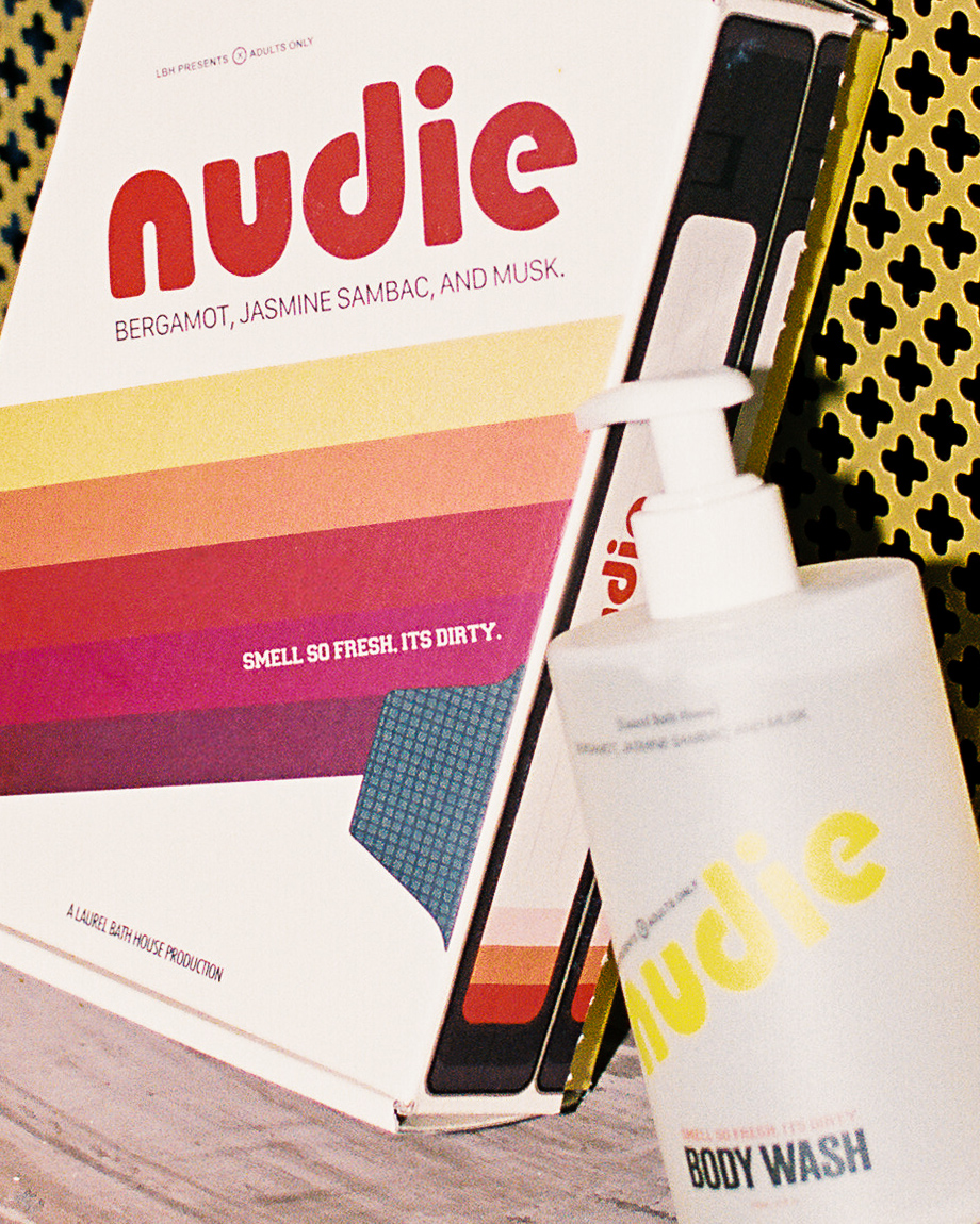 A box with the word 'nudie' and a bottle of body wash in front of it, with a yellow and black background.