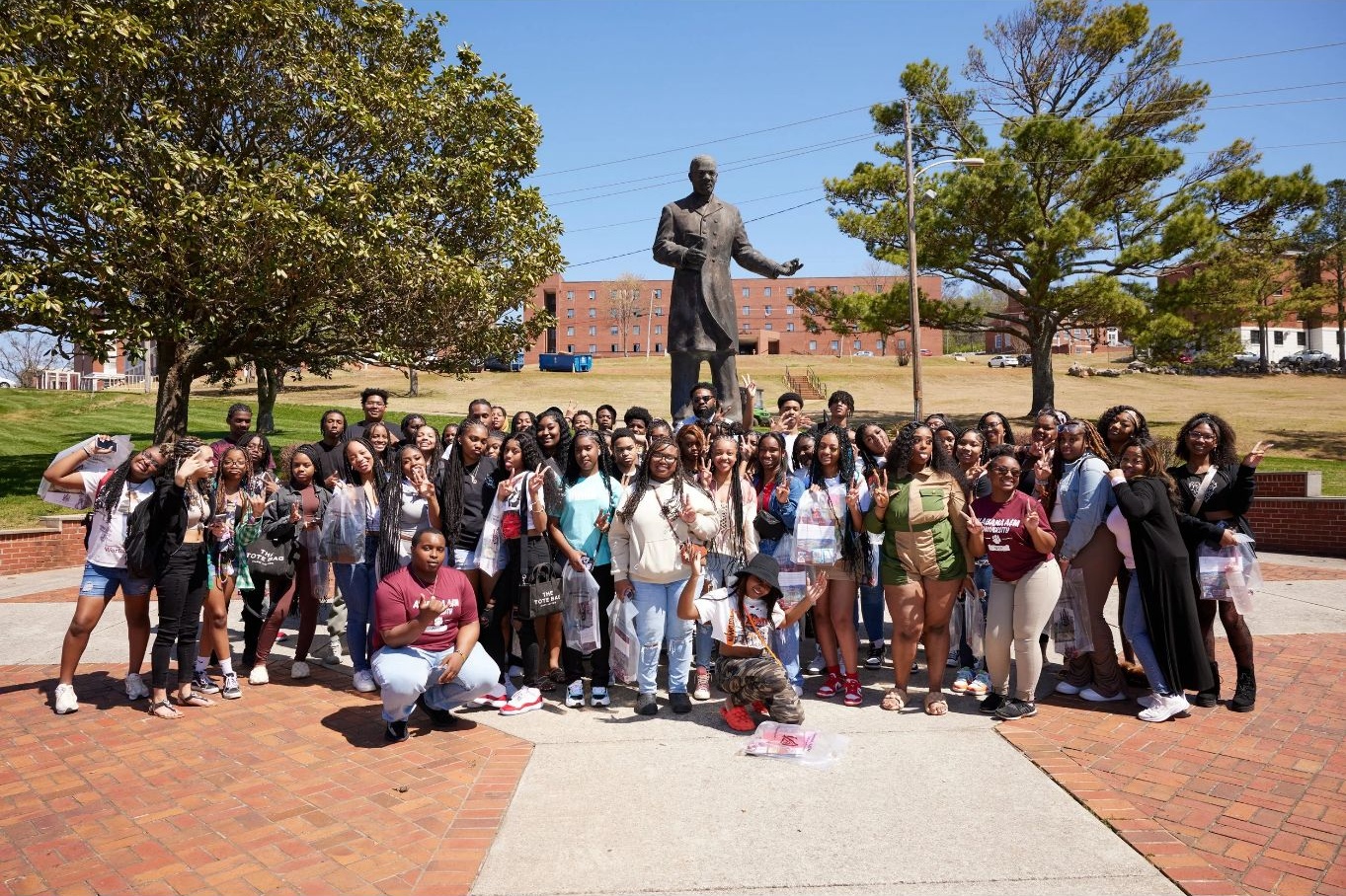 Group of people standing in front of a statue surrounded by trees and a brick walkway.