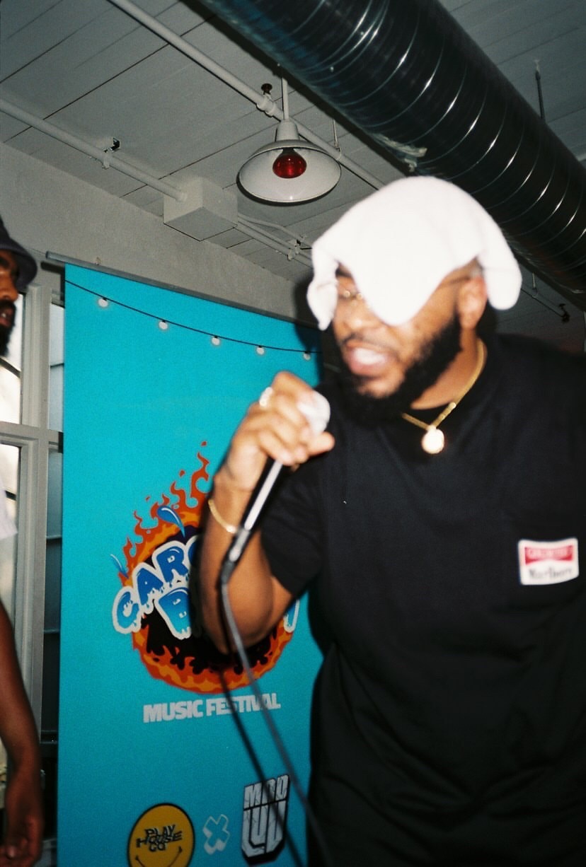 Person holding a microphone with a white cloth over their eyes, standing in front of a blue banner at an indoor event.