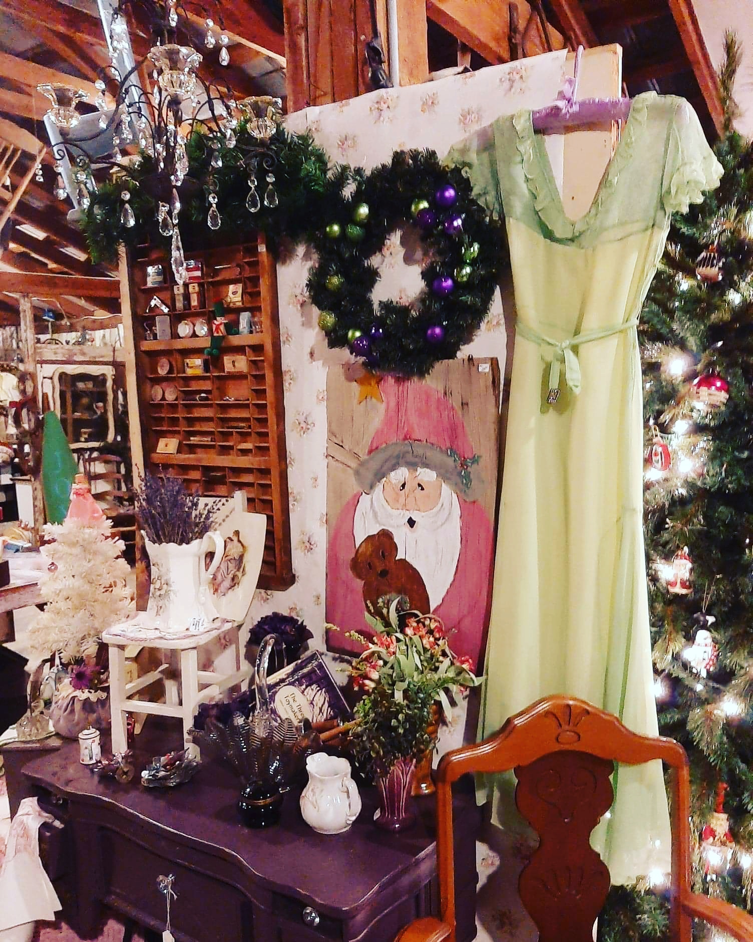 Decorated room with Christmas wreath, yellow dress, and festive ornaments on a table, with a Christmas tree in the background.