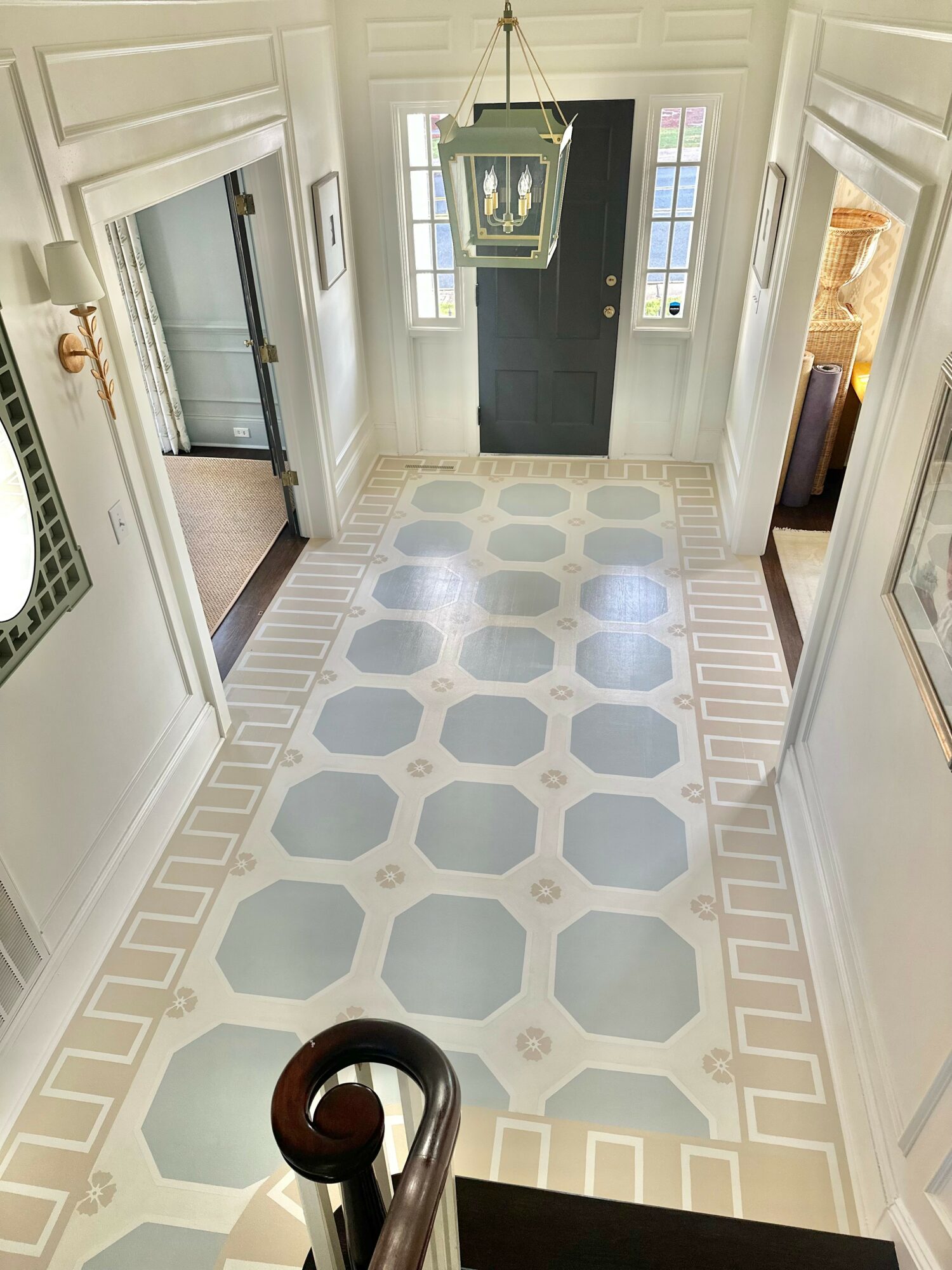 View of a hallway with patterned tile floor, chandelier, front door, and windows, seen from above.