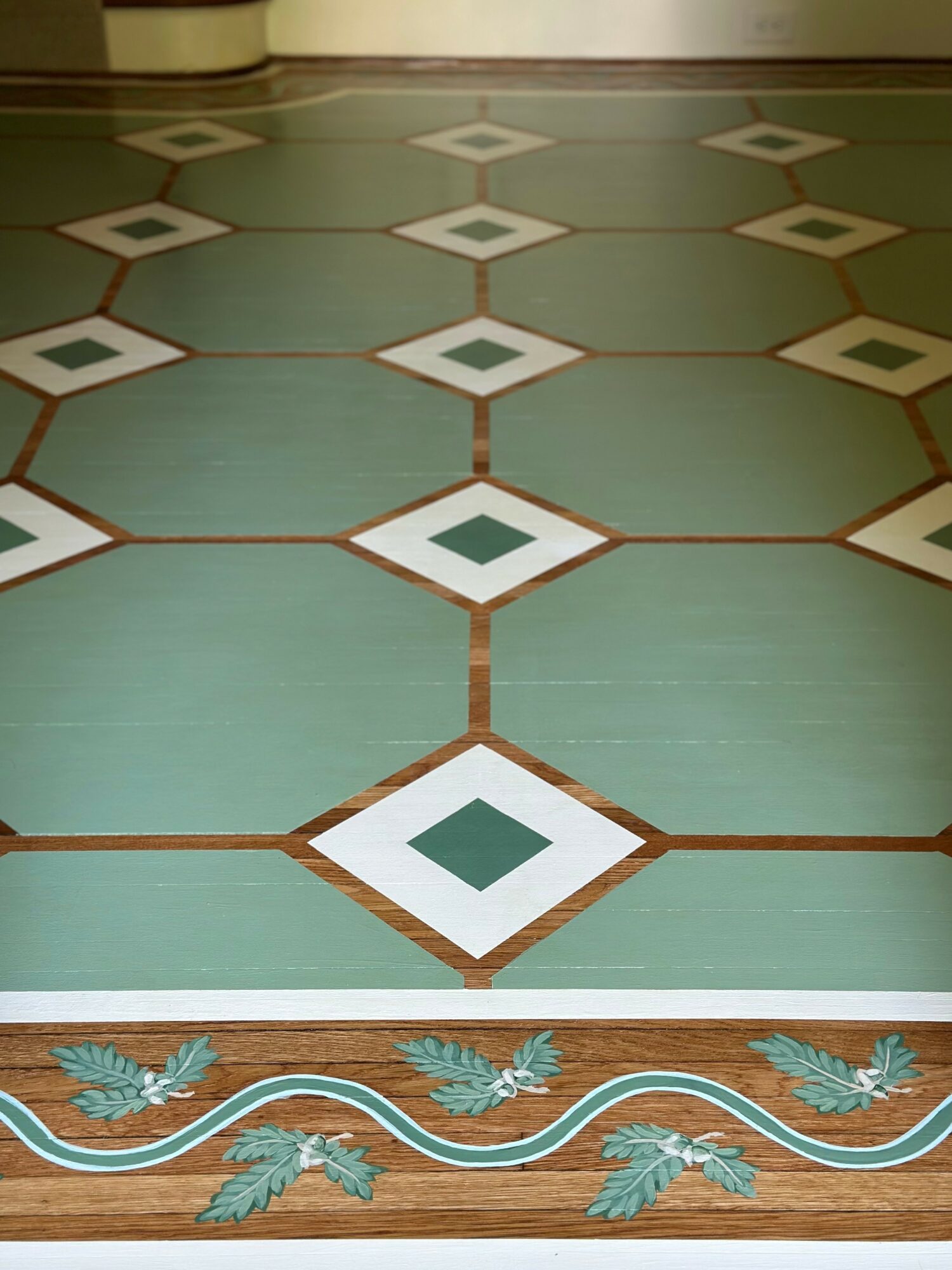 Floor with large green tiles and decorative border featuring blue leaves and white wavy lines.