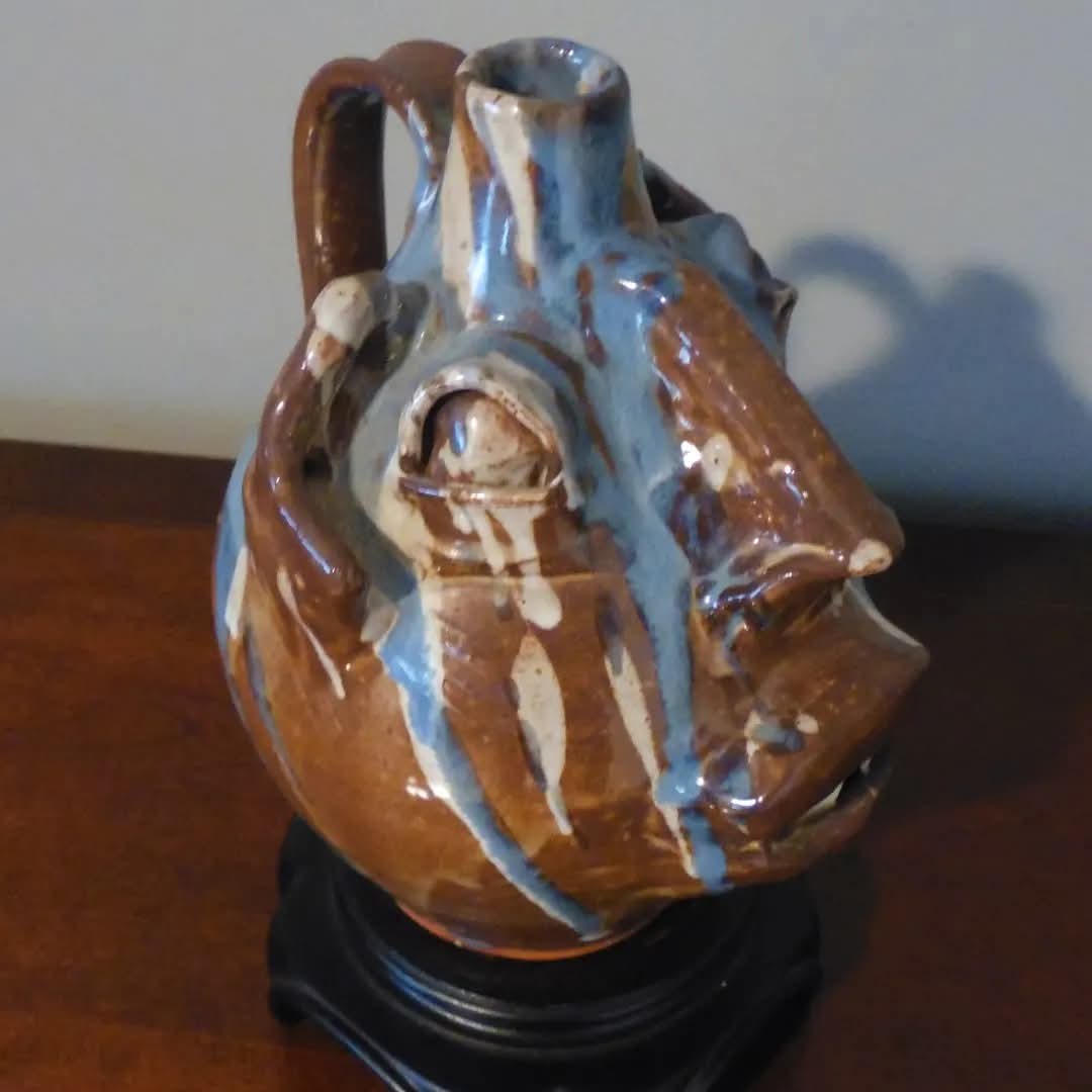 Ceramic pitcher with brown and blue glaze, placed on a black stand on a wooden surface.