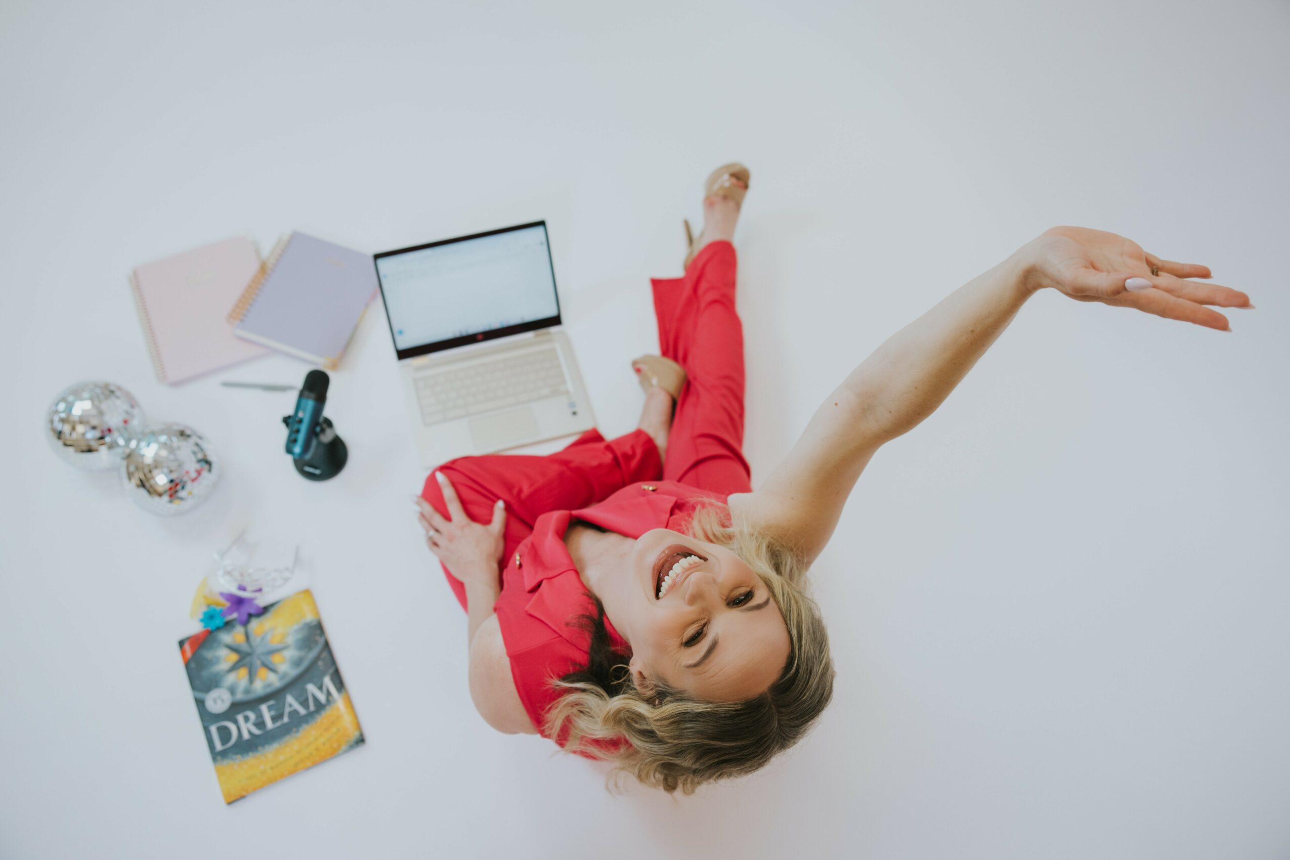 Woman lying on the floor with arms outstretched, surrounded by a laptop, notebooks, and decorative items.