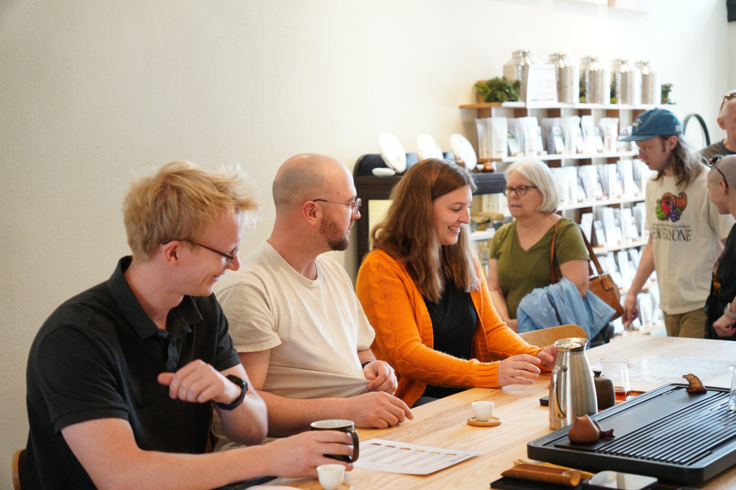 People sitting at a table in a store, engaging in conversation, with shelves of products in the background.