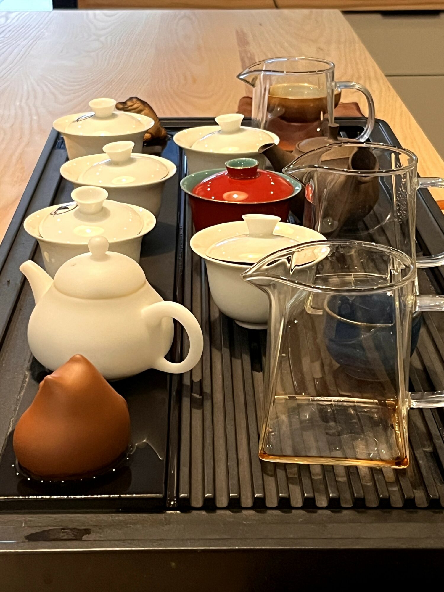Tea set with teapots, cups, and glass pitchers on a black tray on a wooden table, with a brown object in the foreground.