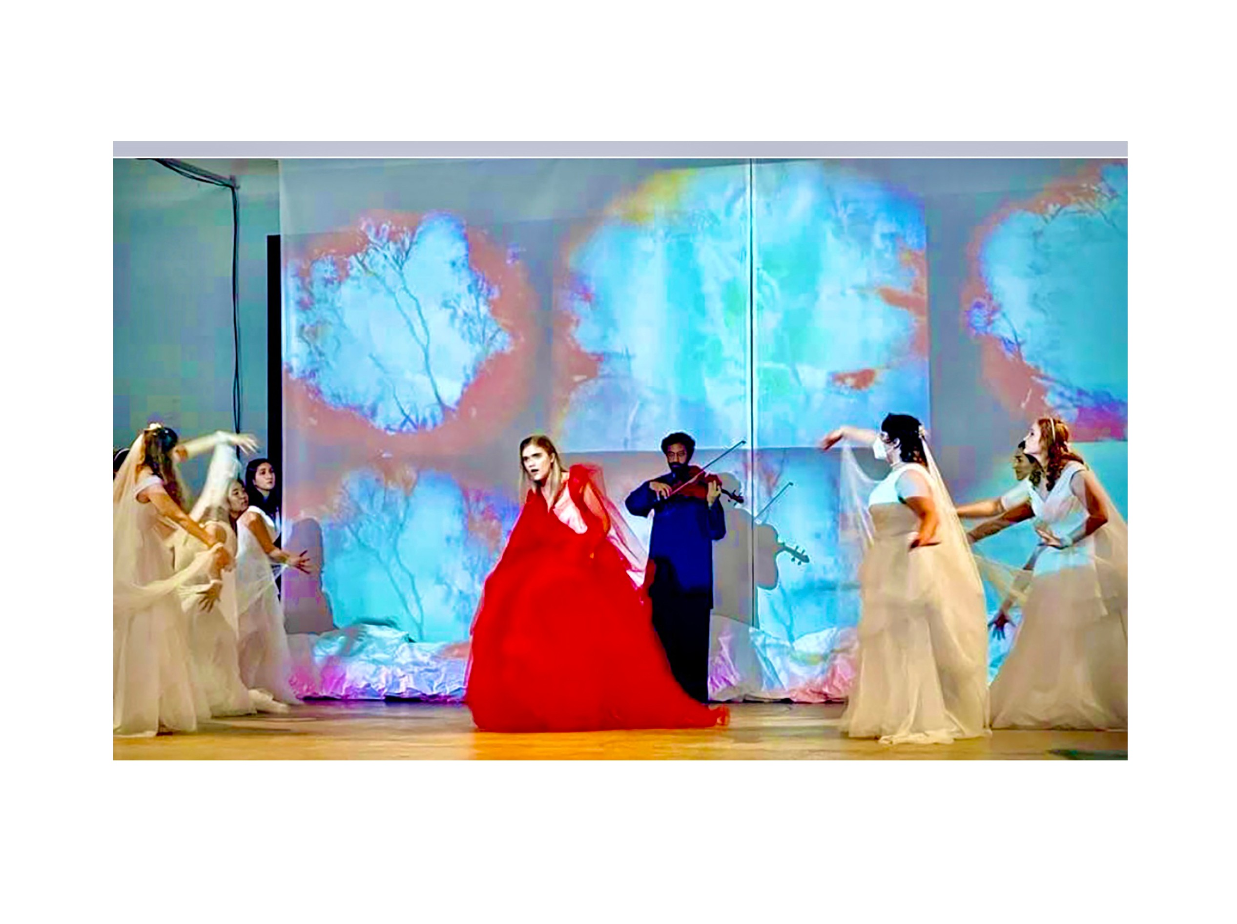 Group of people performing on stage with colorful background, one person in a red dress center, others in white dresses.