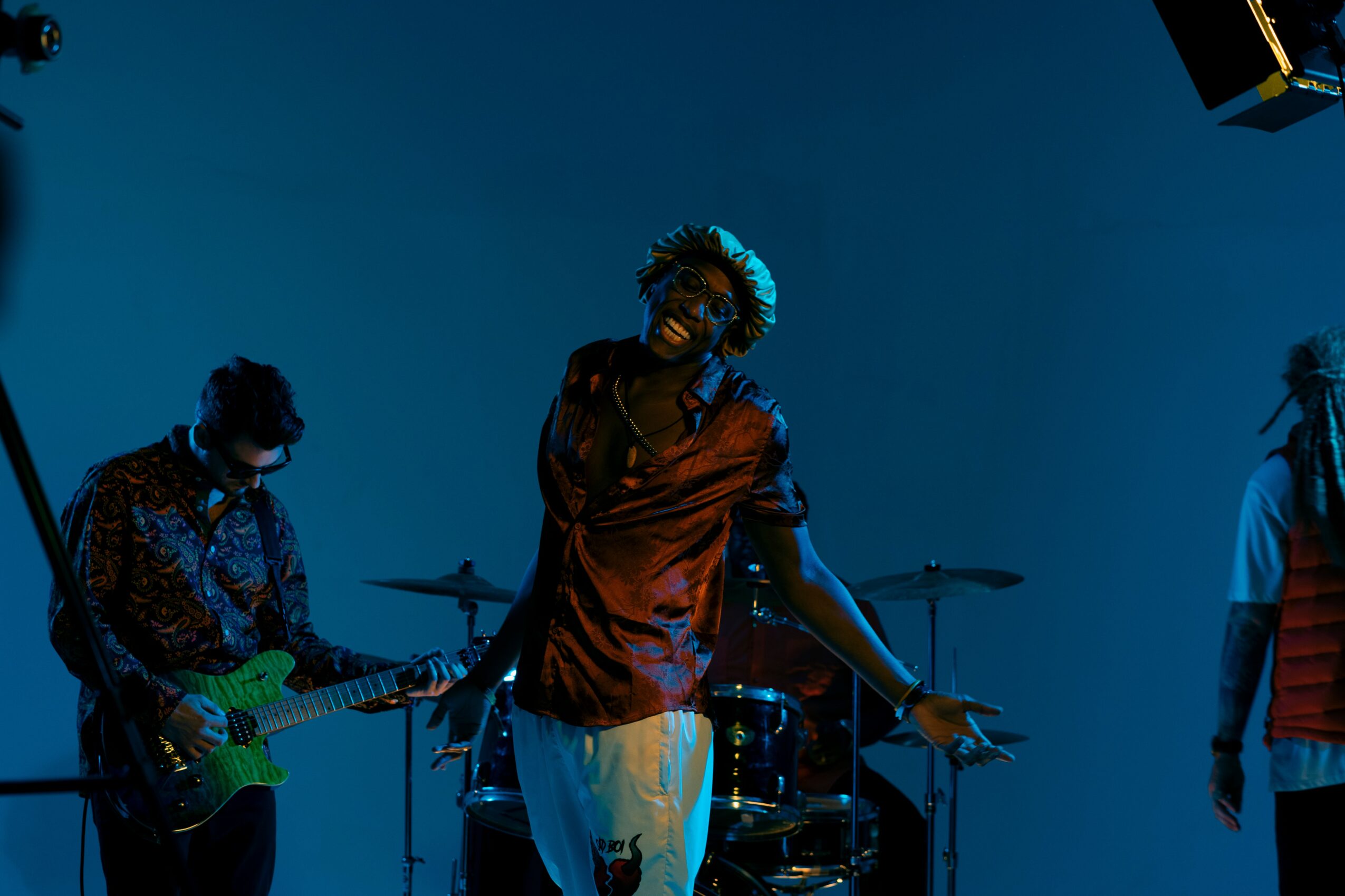 Three musicians perform on stage with blue lighting, one singing and two playing instruments.