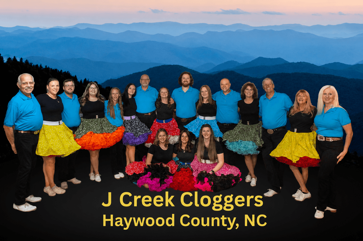 Group of people outdoors with mountains in background, wearing colorful skirts and blue shirts, smiling, with text about J Creek Cloggers in NC.