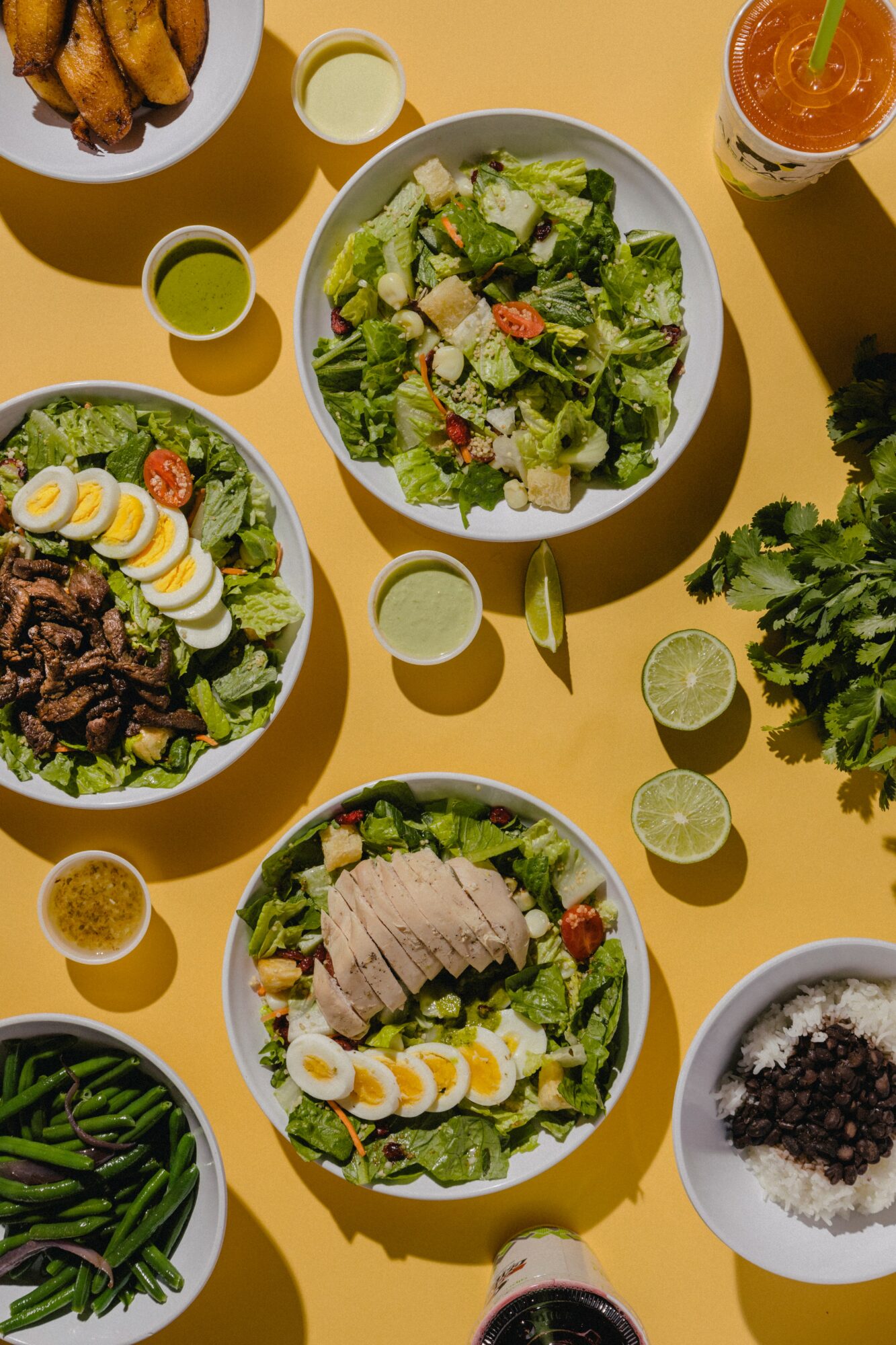 Assorted dishes including salad, rice, and vegetables on a yellow table, with drinks and small bowls.