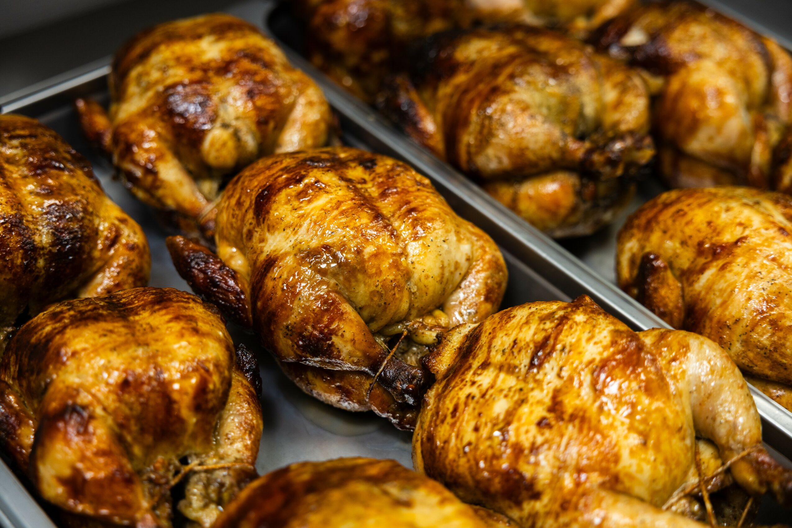 Several roasted chickens on a tray with golden-brown crispy skin, arranged closely together.