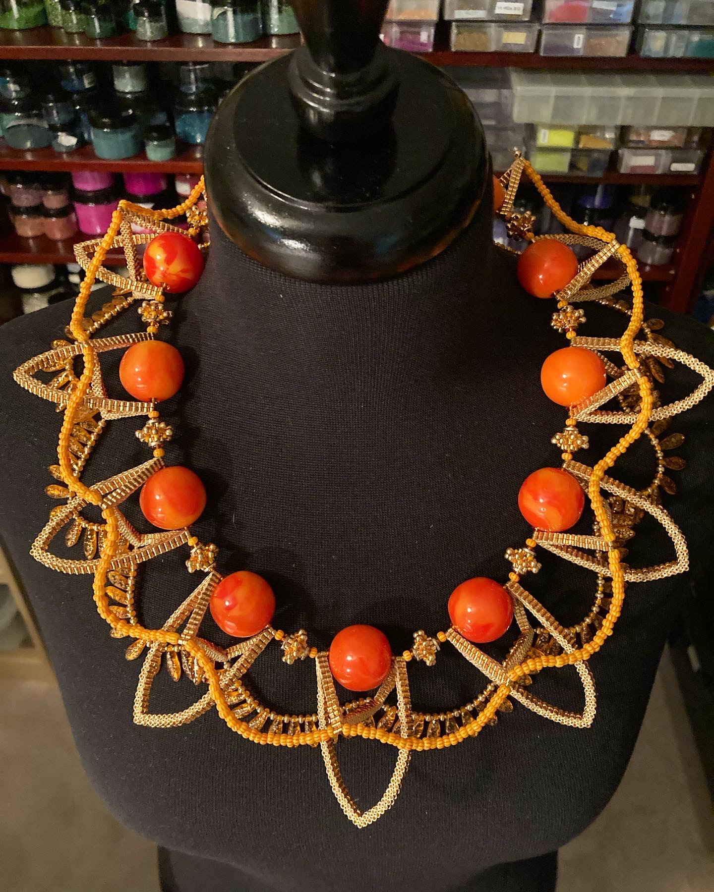 Necklace with large orange beads and intricate gold-colored design displayed on a black mannequin bust.