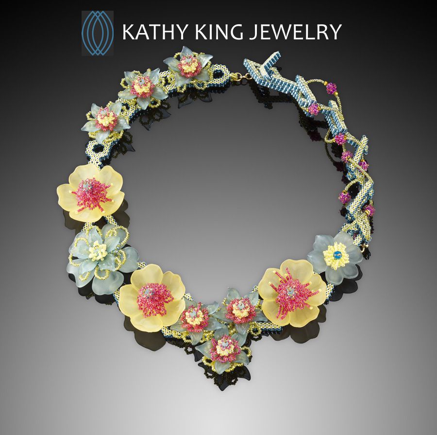 Colorful floral necklace with yellow, pink, and blue flowers, and a beaded twist design, displayed against a dark background.