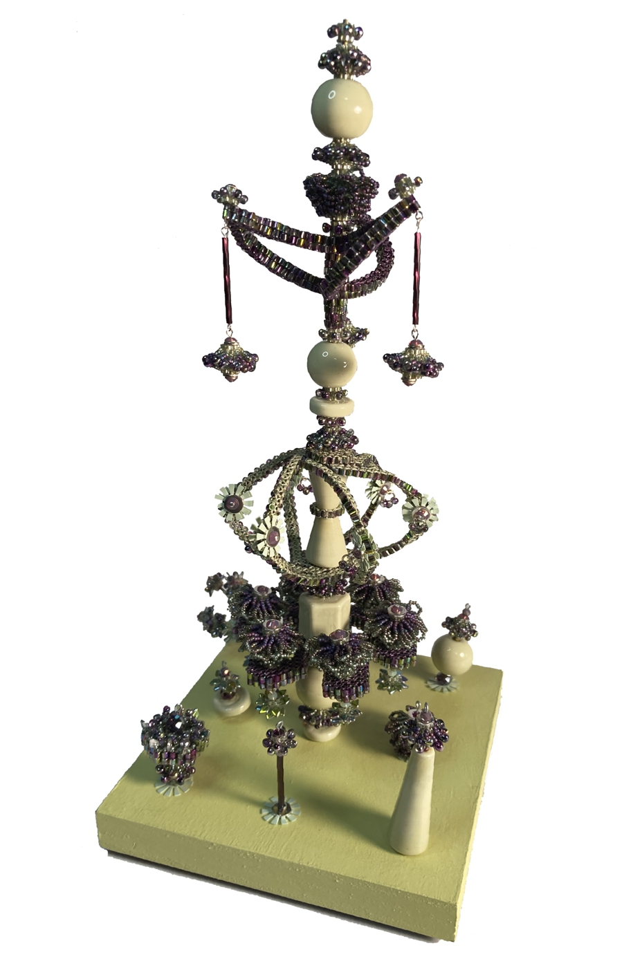 Decorative object with beads, chains, and ornaments on a green base, featuring a tall vertical structure with hanging elements.