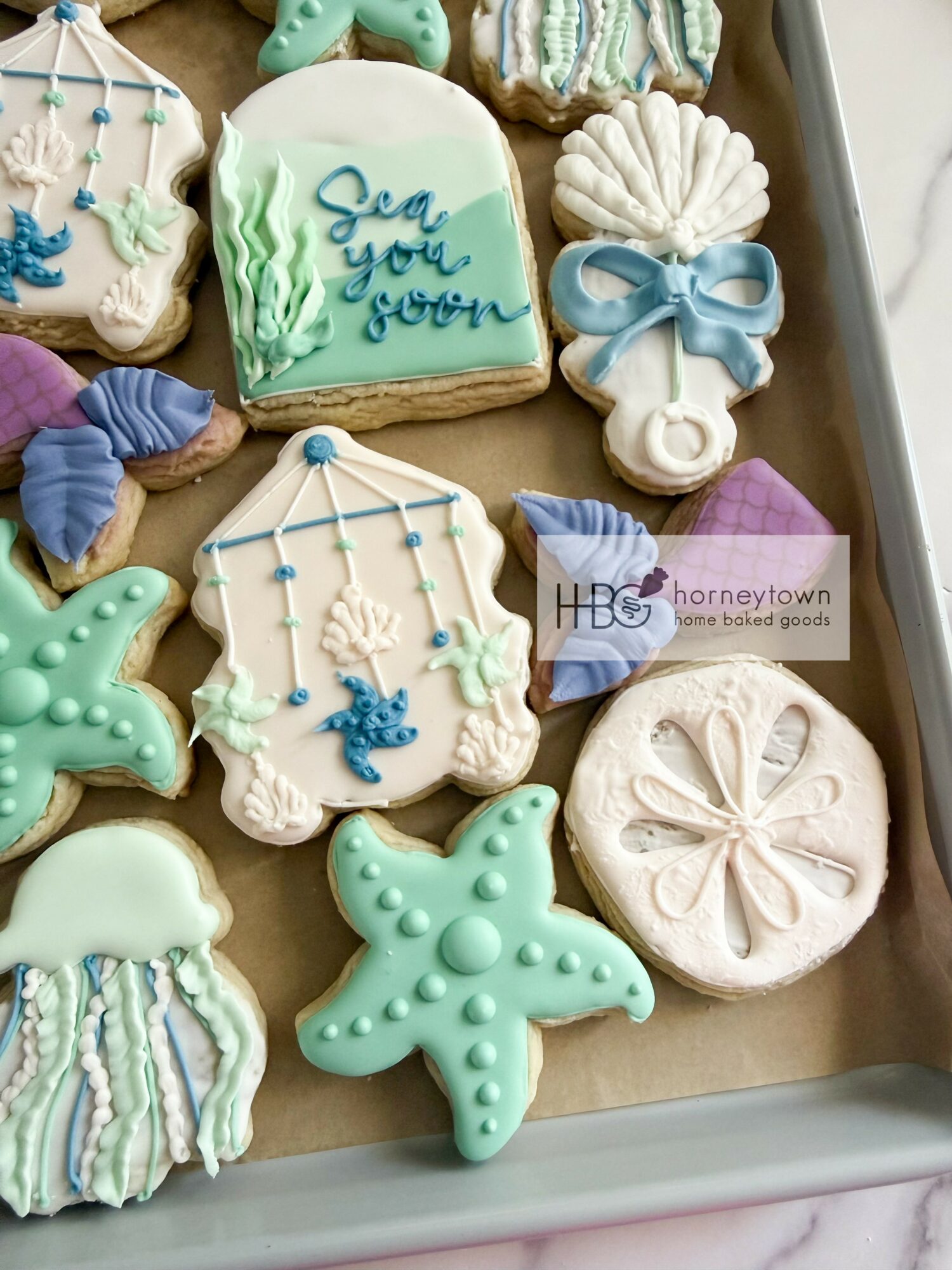 Assorted decorated cookies with sea and beach themes, including shells, starfish, and a message cookie, on a tray.