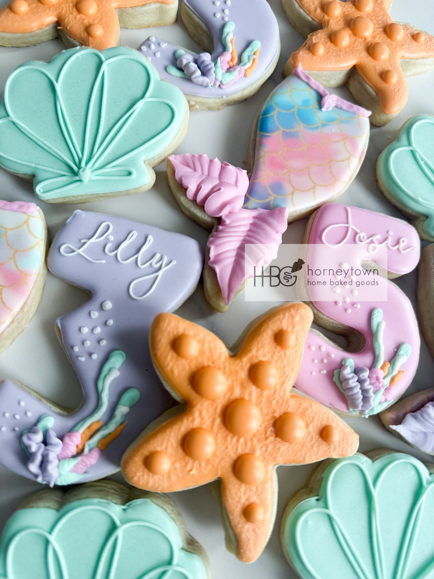 Decorated cookies with seashell, starfish, unicorn, rainbow, and cloud shapes in pastel colors.