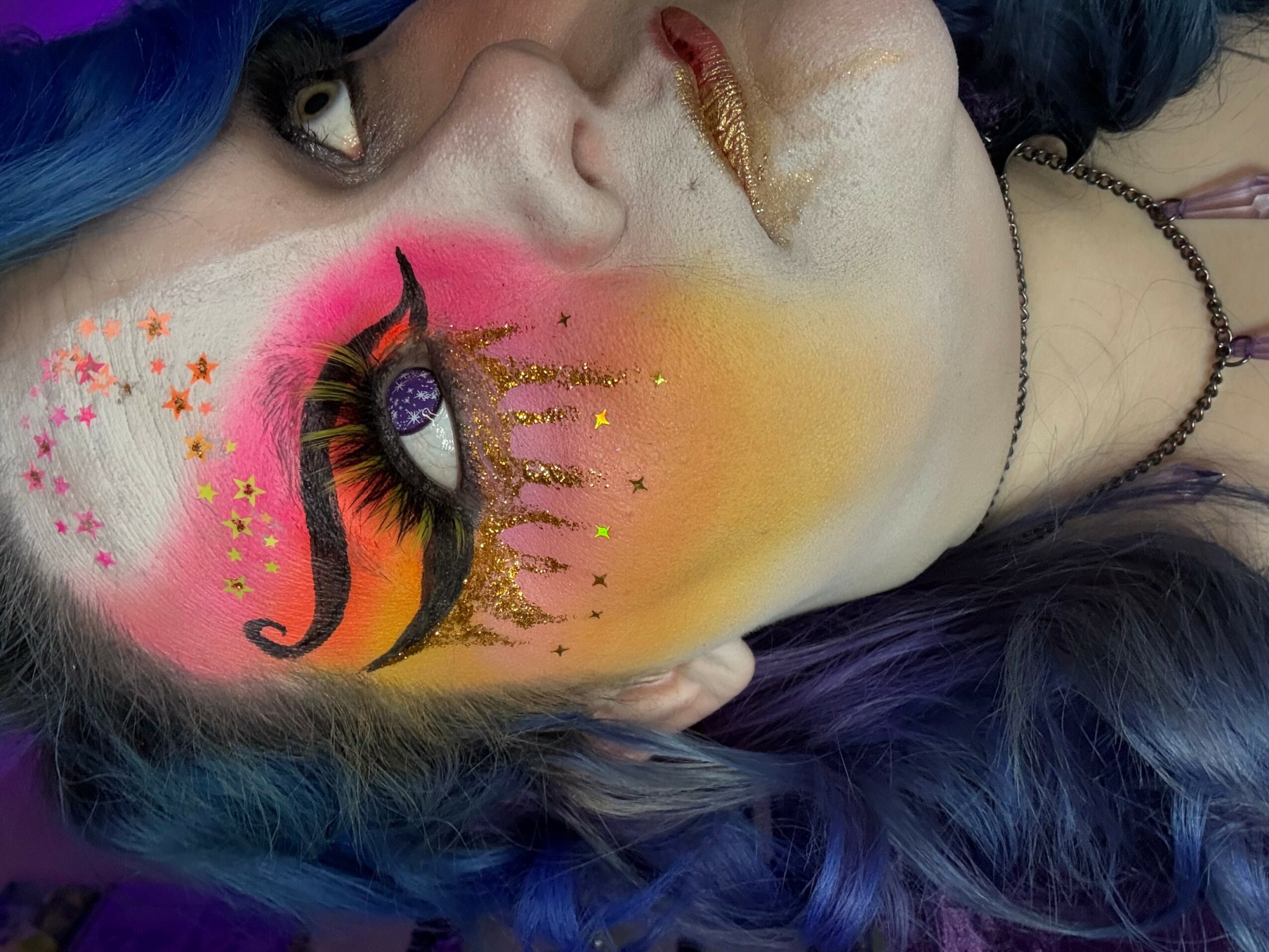 Close-up of a person's face with colorful face paint, including a unicorn and stars, and vibrant blue hair.