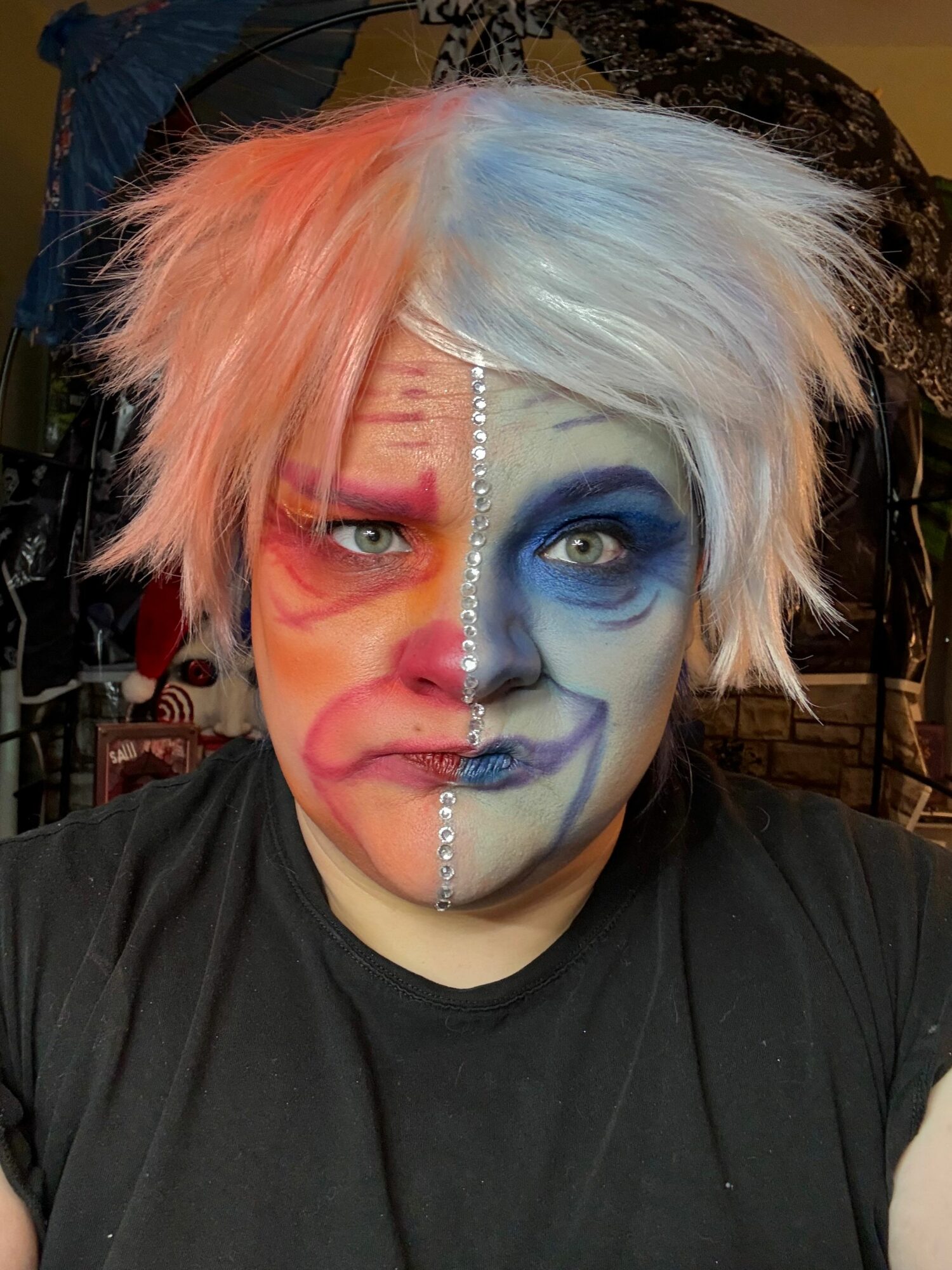 Person with colorful makeup and hair, wearing a black shirt, facing sideways.