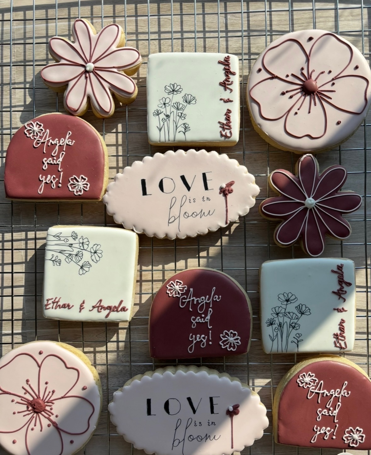 Decorative cookies with floral and love-themed designs in a wire basket, some with names and messages, on a grid surface.