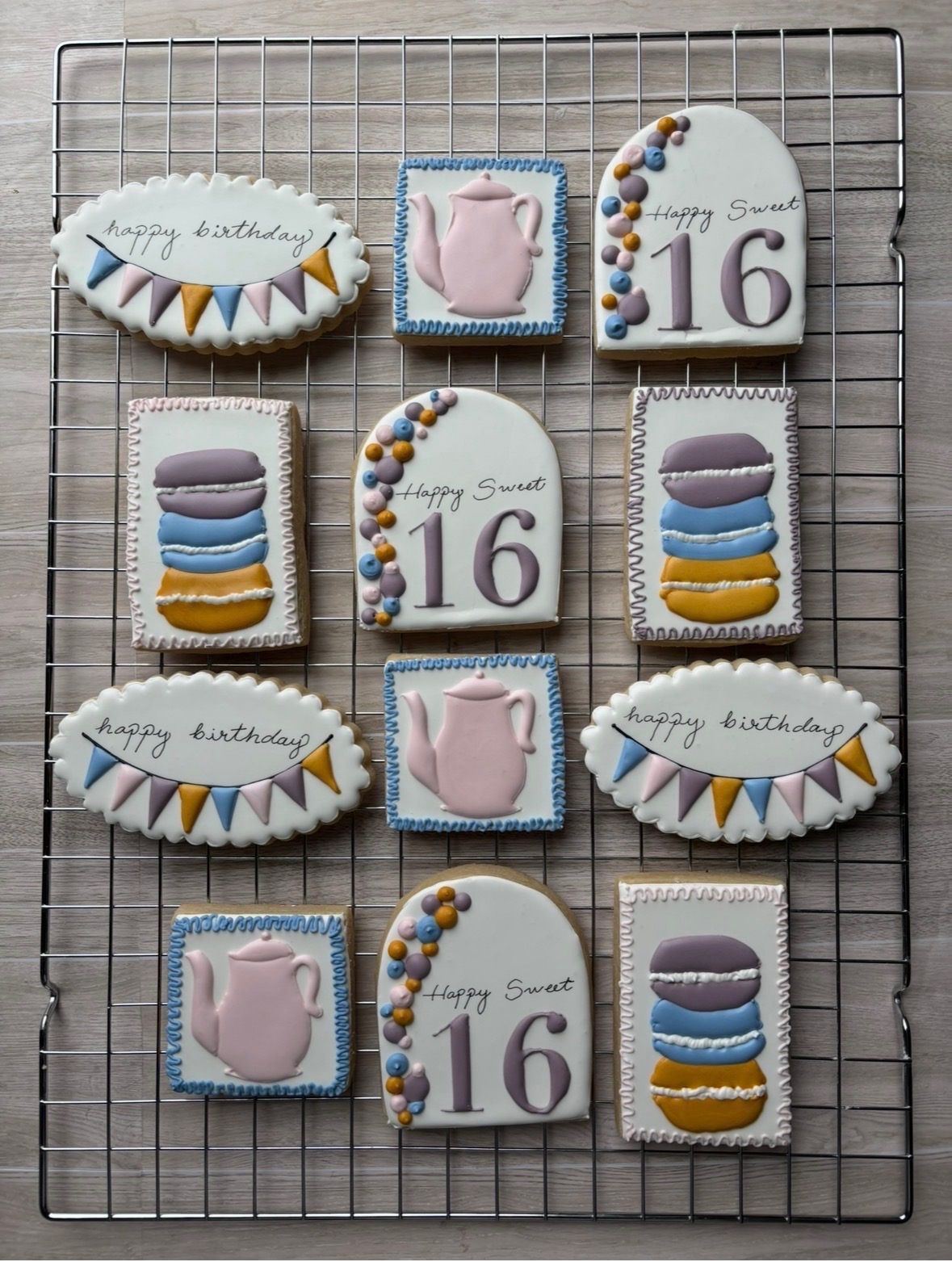 Decorative birthday cookies on a cooling rack, including a cake, teapot, and number 16, with birthday messages.