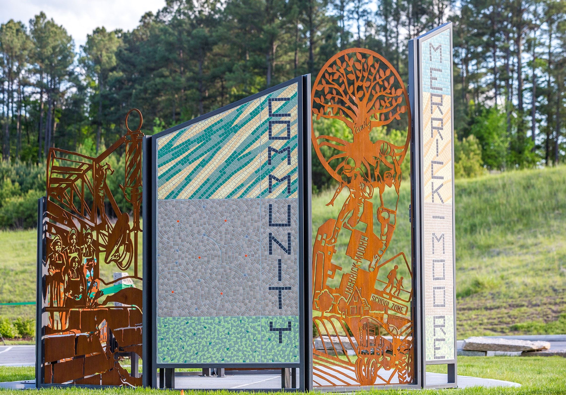 Four colorful panels with trees, patterns, and text, set outdoors with trees and grass in the background.