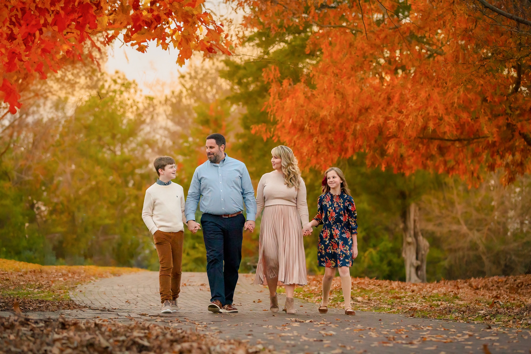 Four people walking on a path in a park with autumn trees and colorful leaves, holding hands and talking.
