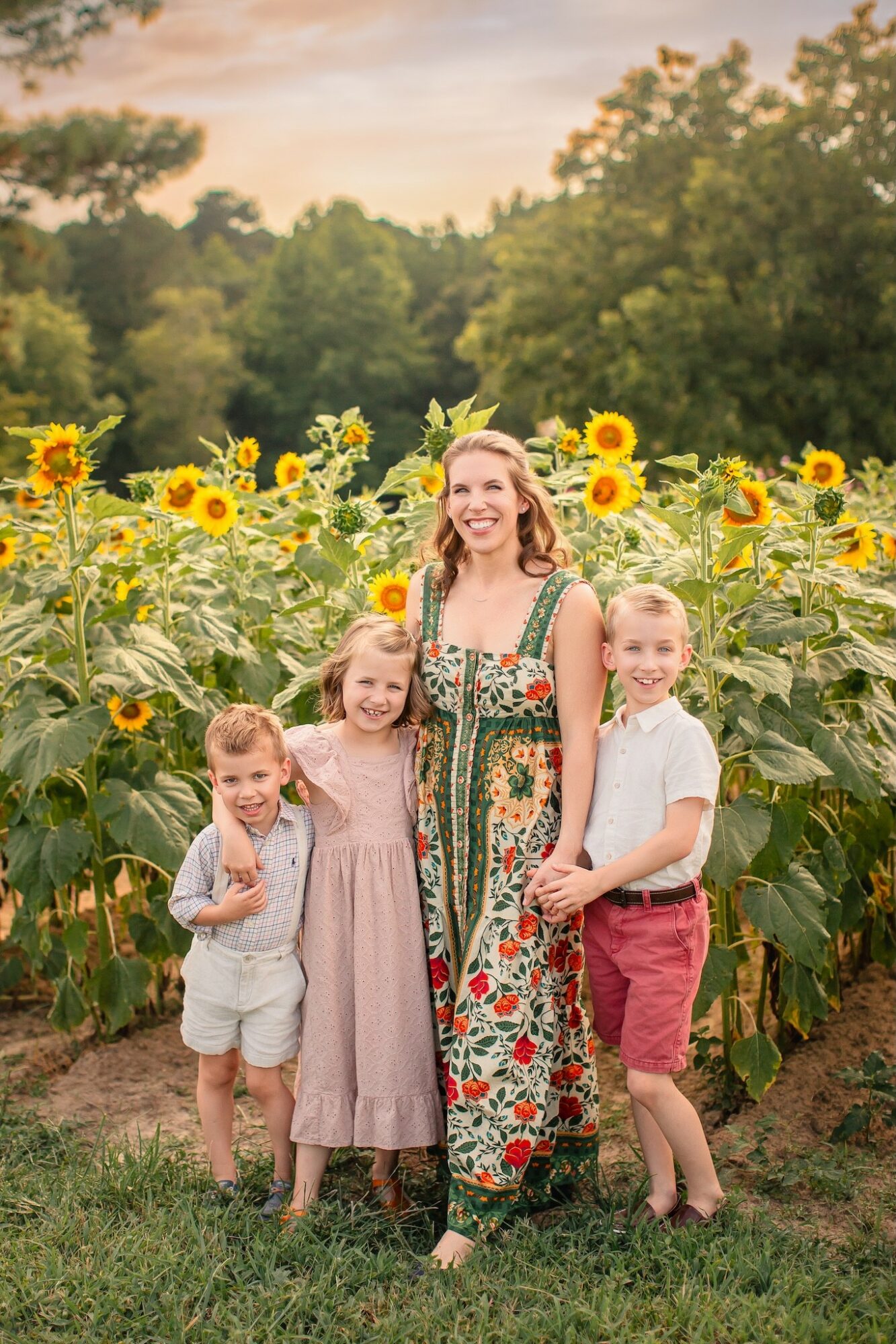 A woman and three children standing in a sunflower field during sunset, smiling and posing for the photo.