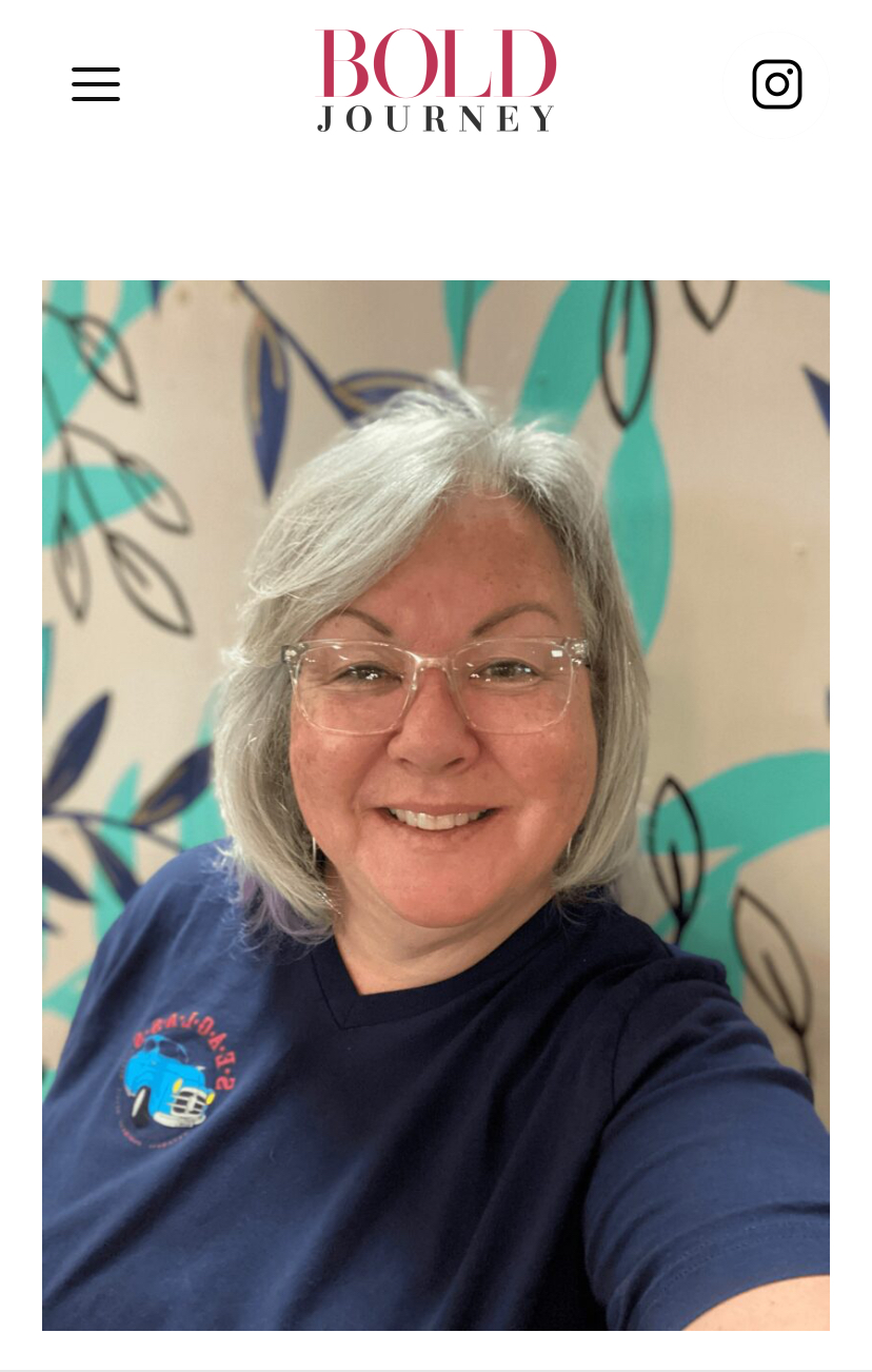 Smiling woman with glasses and gray hair in front of a colorful, abstract background, wearing a dark blue shirt.