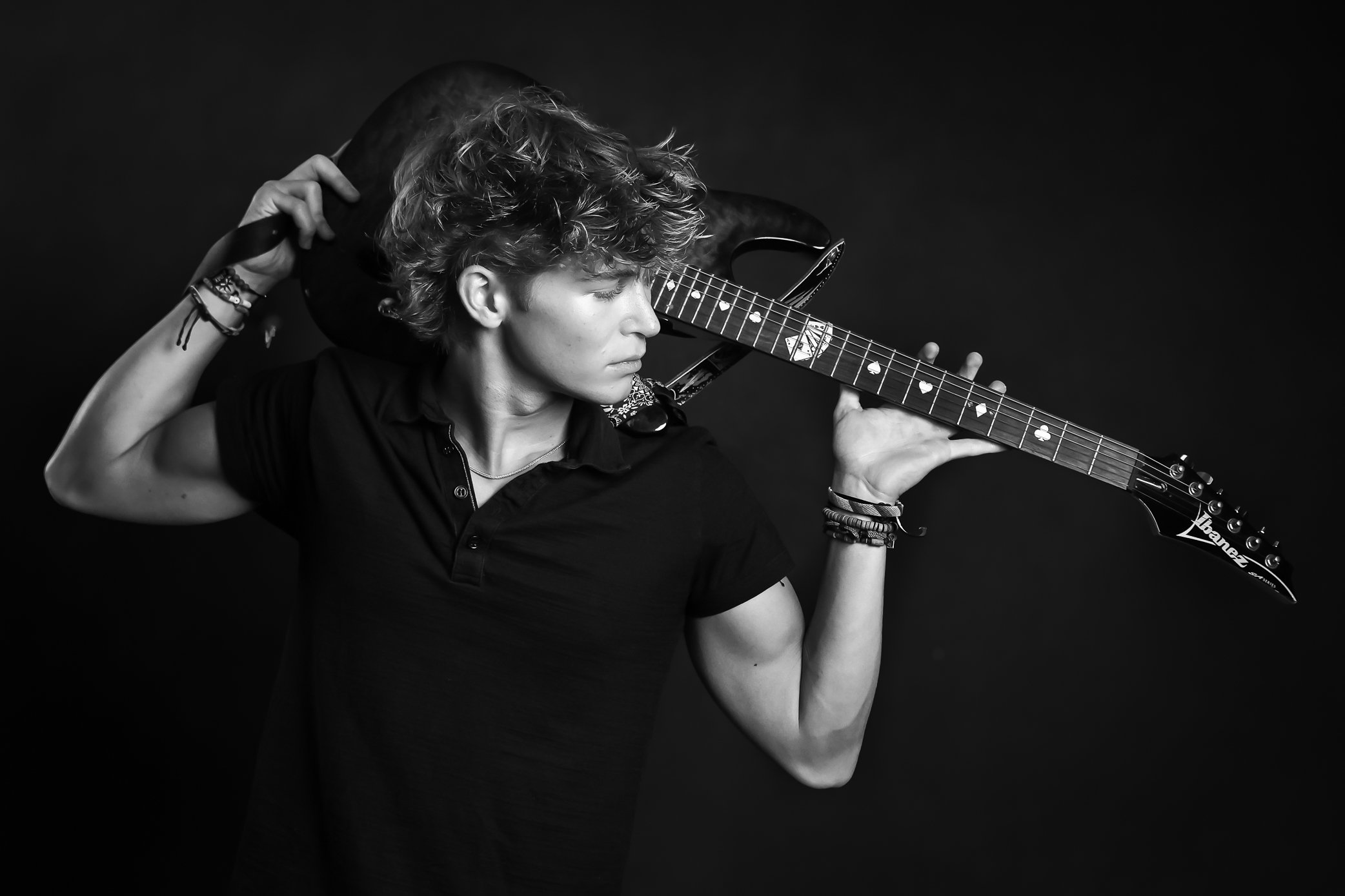 Young person with curly hair holding an electric guitar on shoulder, looking to the side, in black and white.