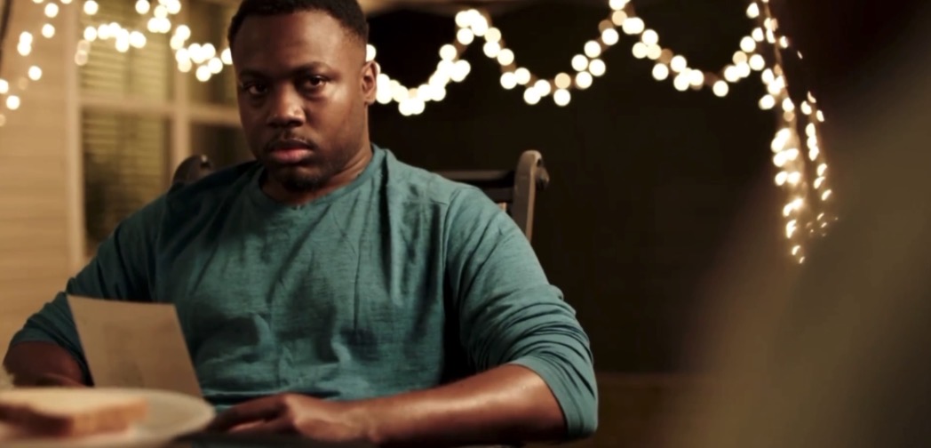 Person sitting at a table with string lights in the background, holding a piece of paper.