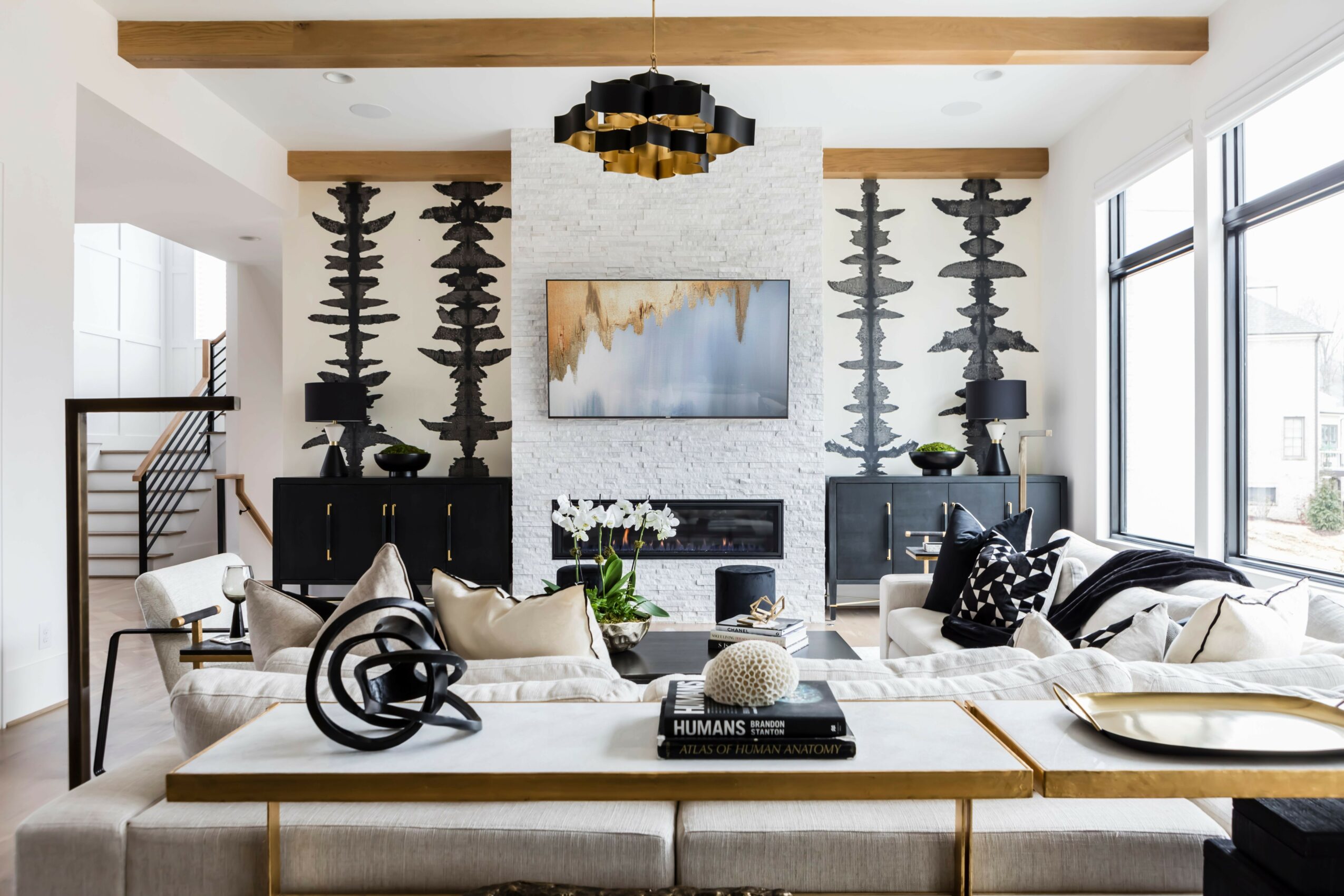 Modern living room with large windows, a fireplace, artwork, and seating area with cushions and decorative objects.